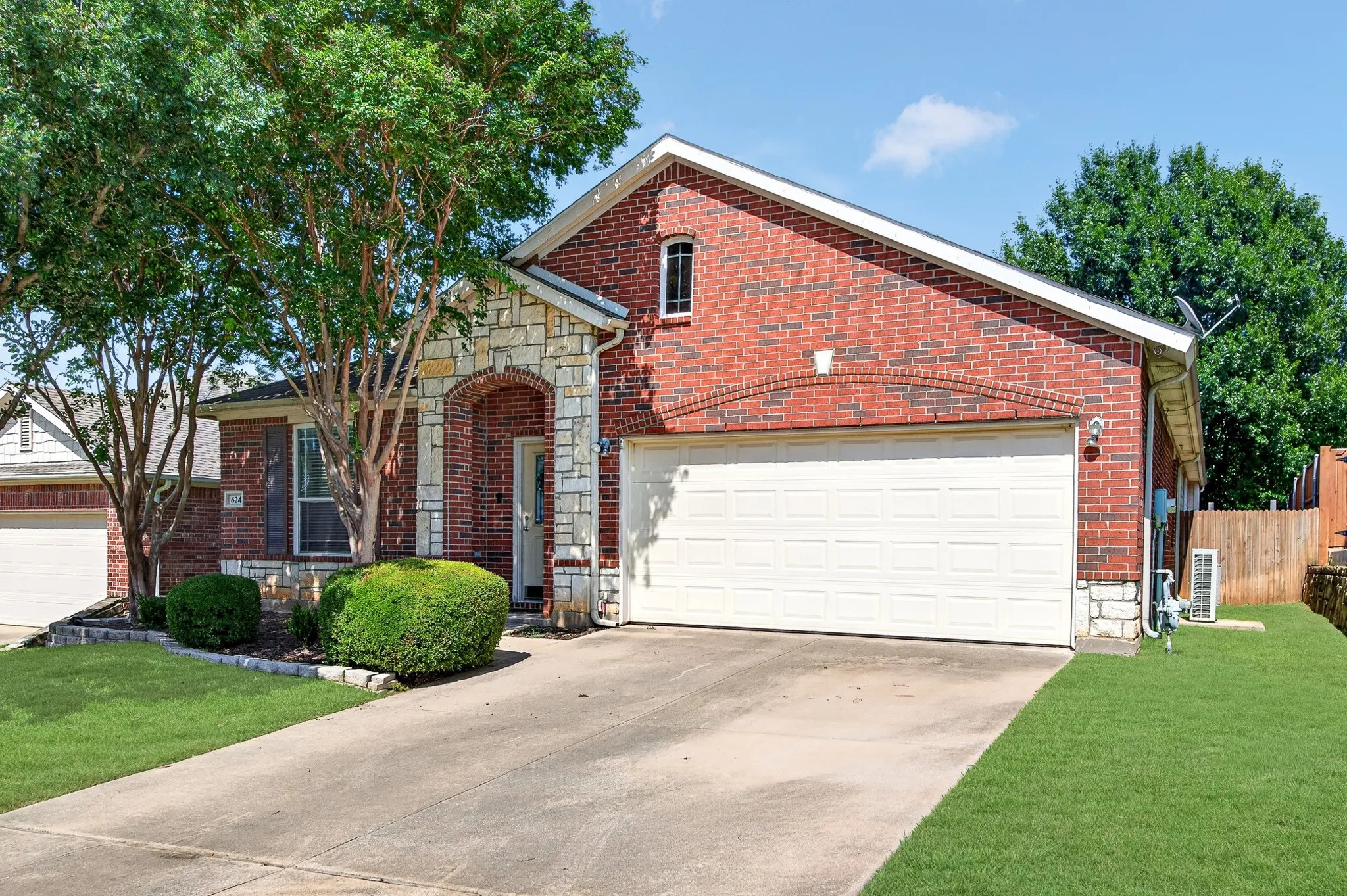 Brick and stone exterior featuring an arched entryway, attached garage with a white garage door, concrete driveway, and established front landscaping