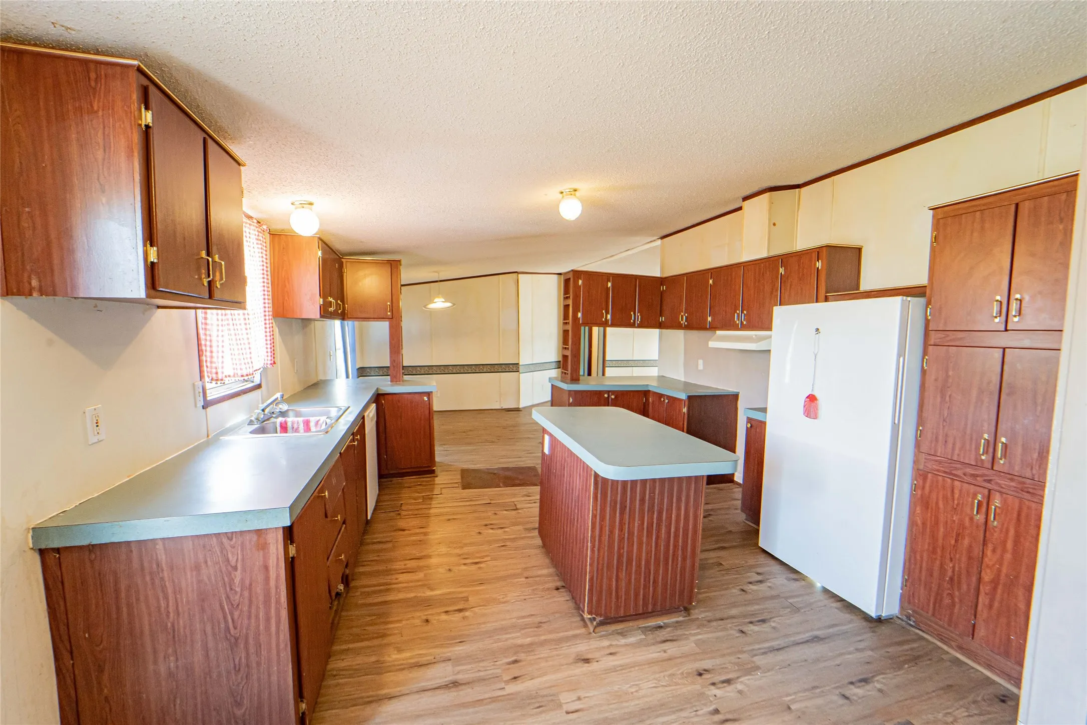 Kitchen featuring wood-finish cabinetry, light blue countertops, a double basin sink, and a central island