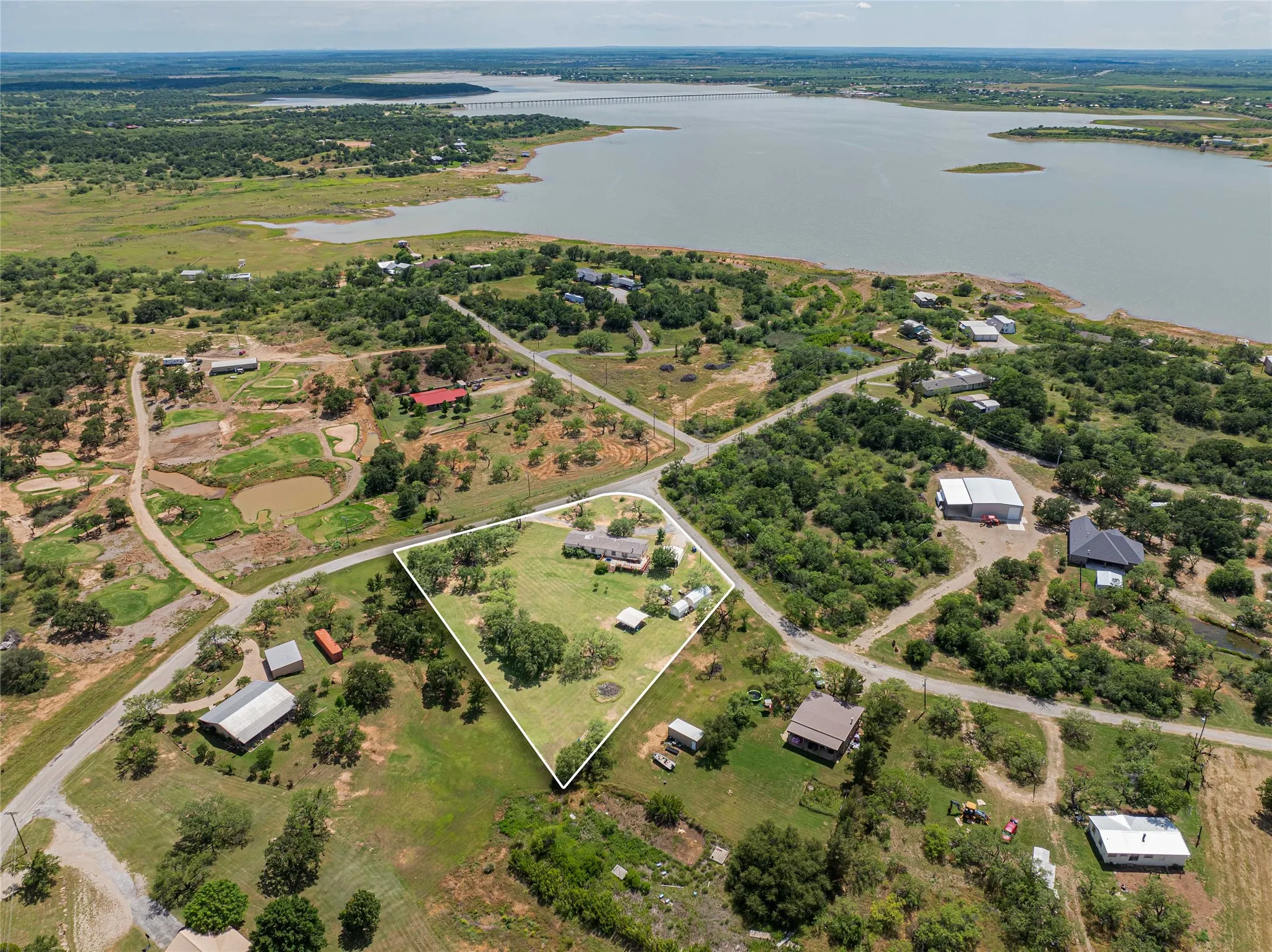 Expansive property featuring a prominent body of water, scattered trees, and a clear boundary outline