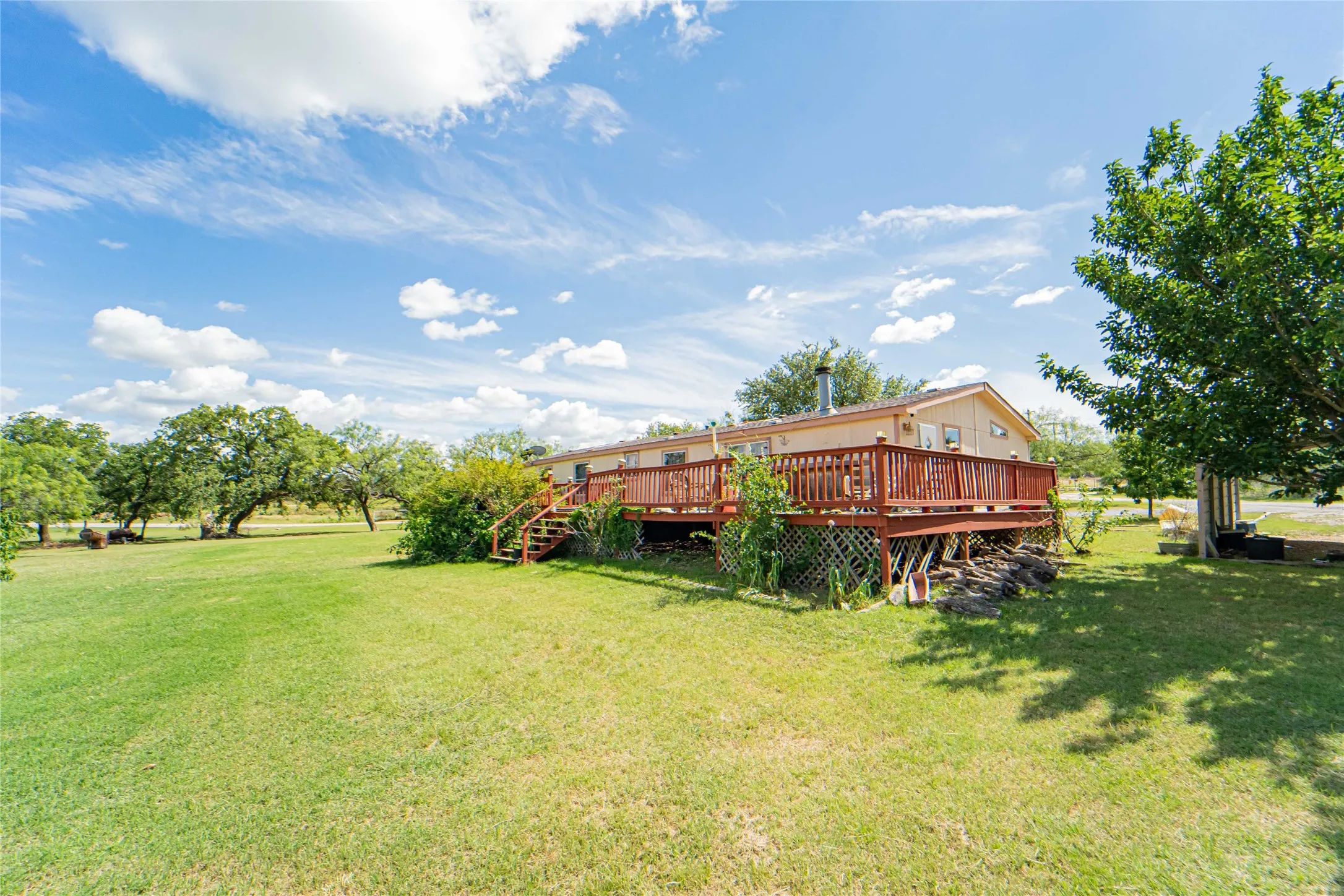 Expansive green lawn bordering a single-story residence with a full-length wooden deck