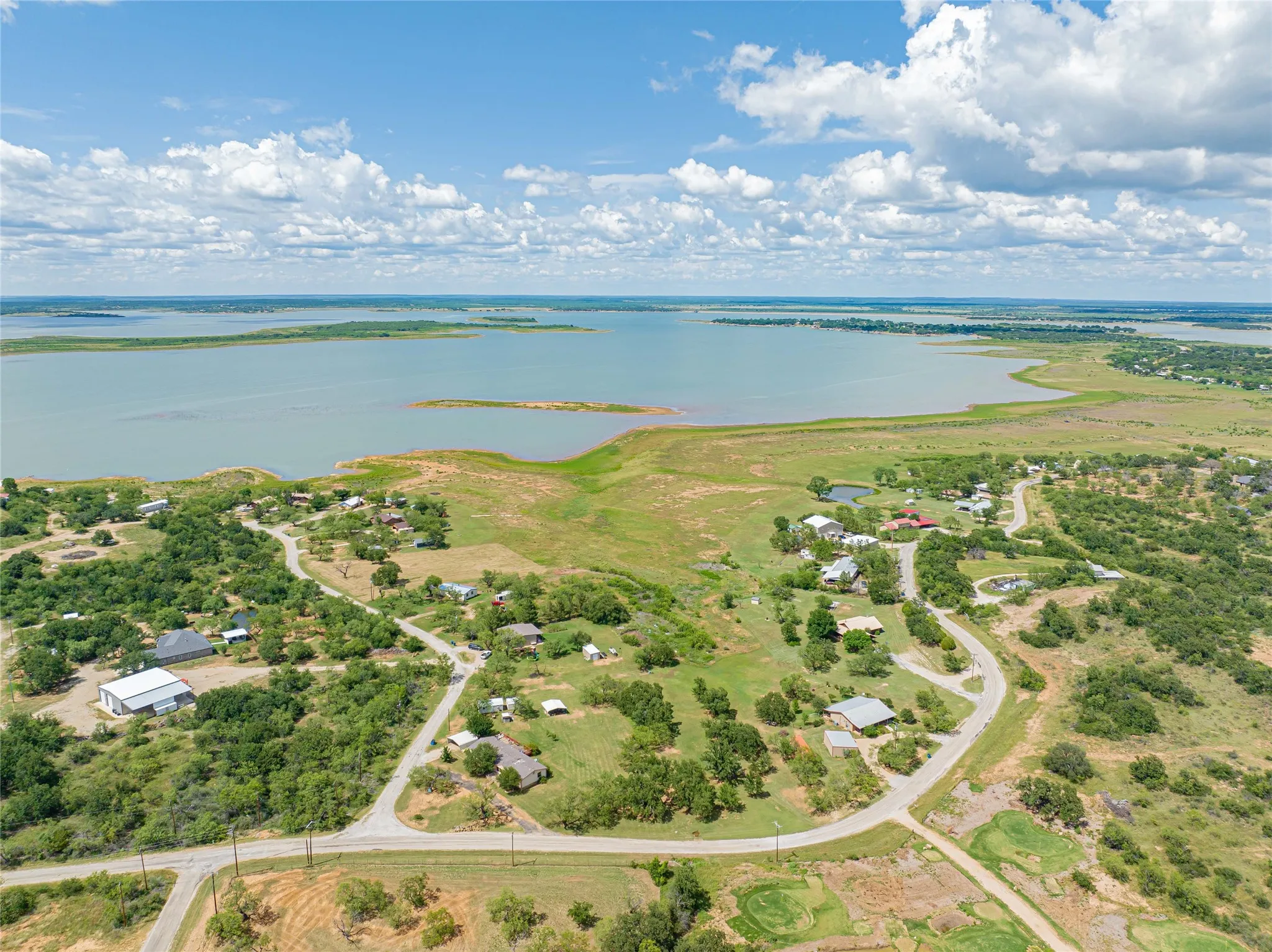 Expansive water body with surrounding land featuring scattered residential structures and diverse tree coverage under a partly cloudy sky