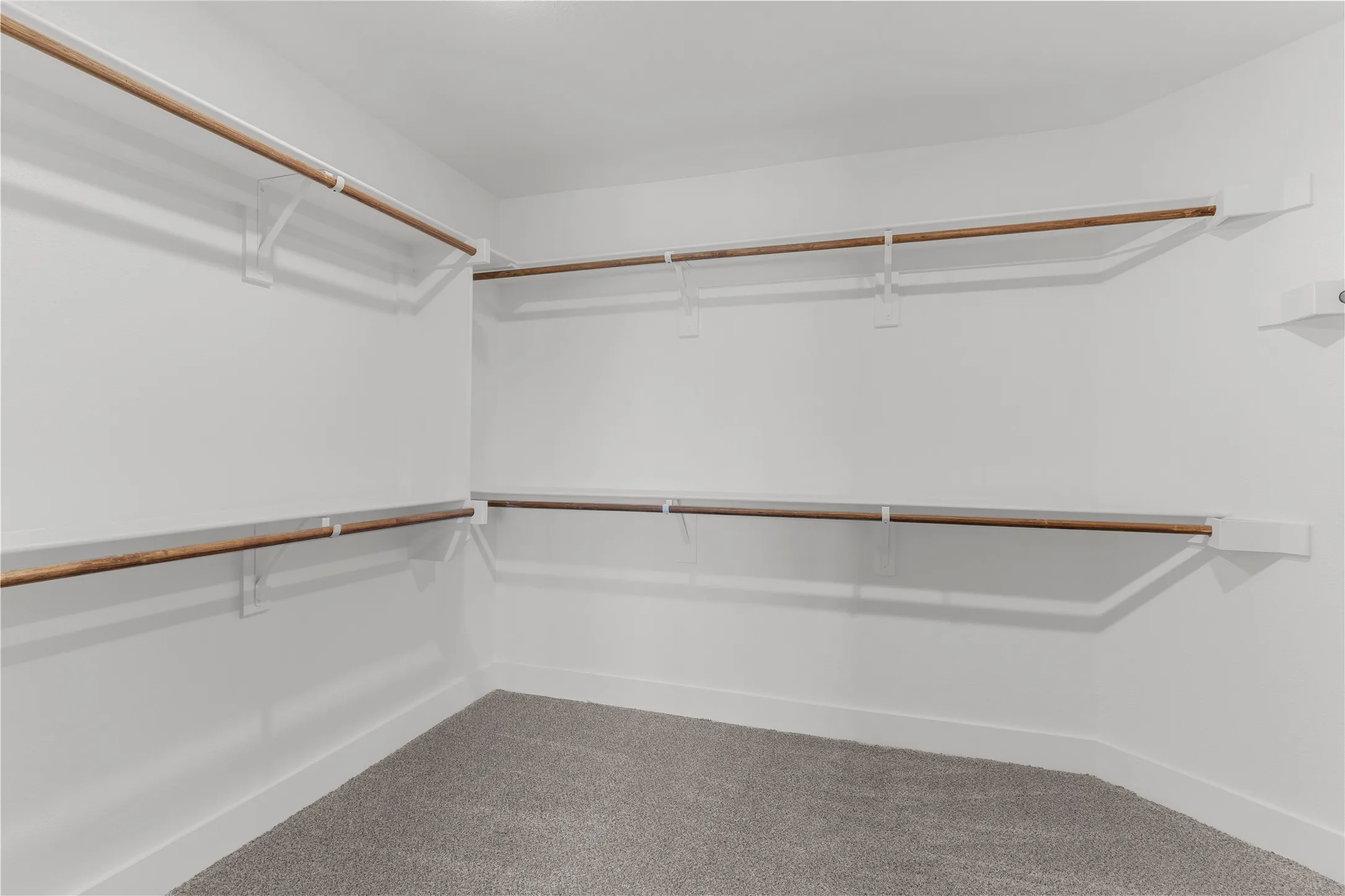 Spacious walk-in closet featuring white walls, white trim, and light wood-finish hanging rods