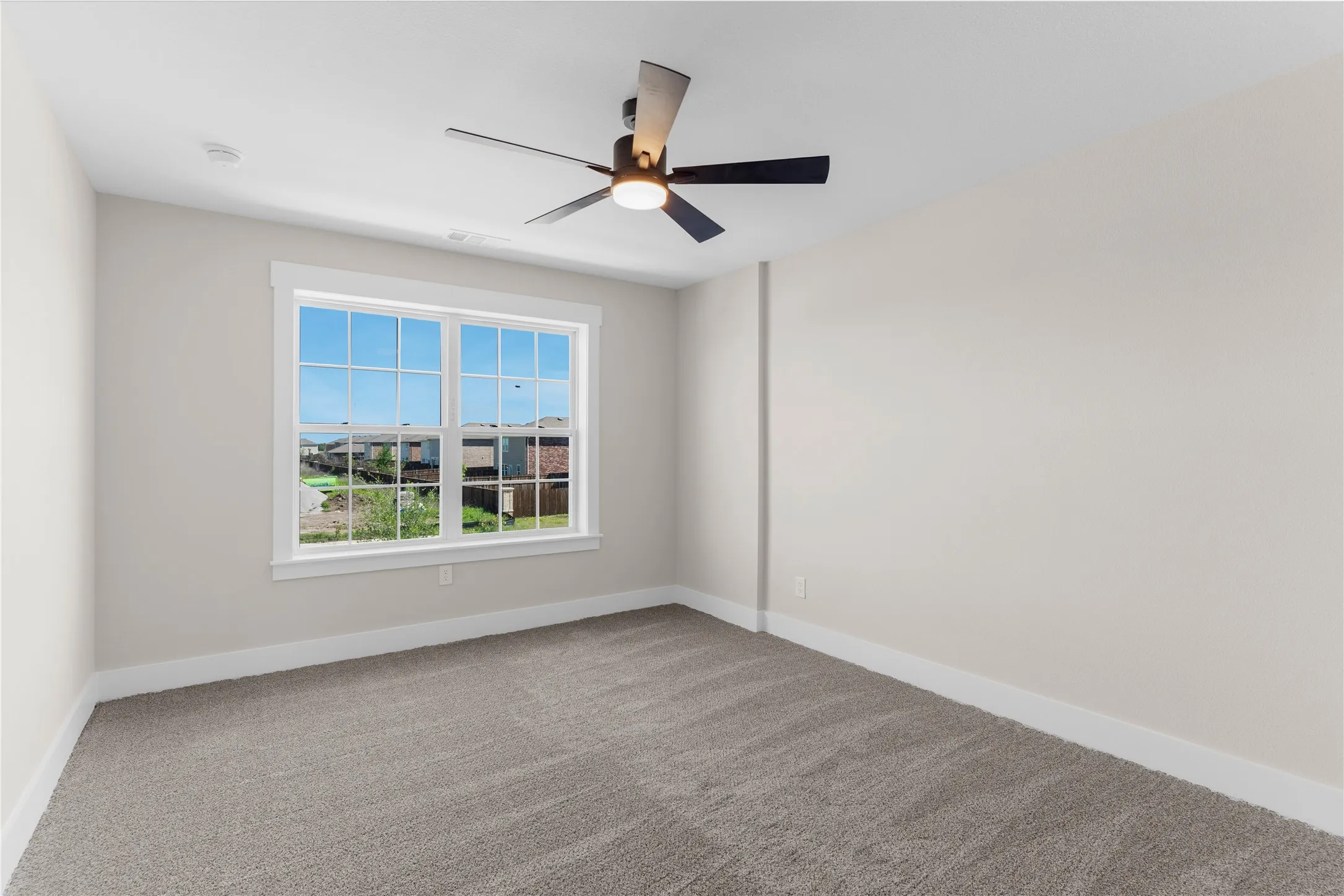 Bright interior room featuring a large window with white trim, neutral carpet flooring, light-colored walls, a ceiling fan with integrated lighting, and white baseboards