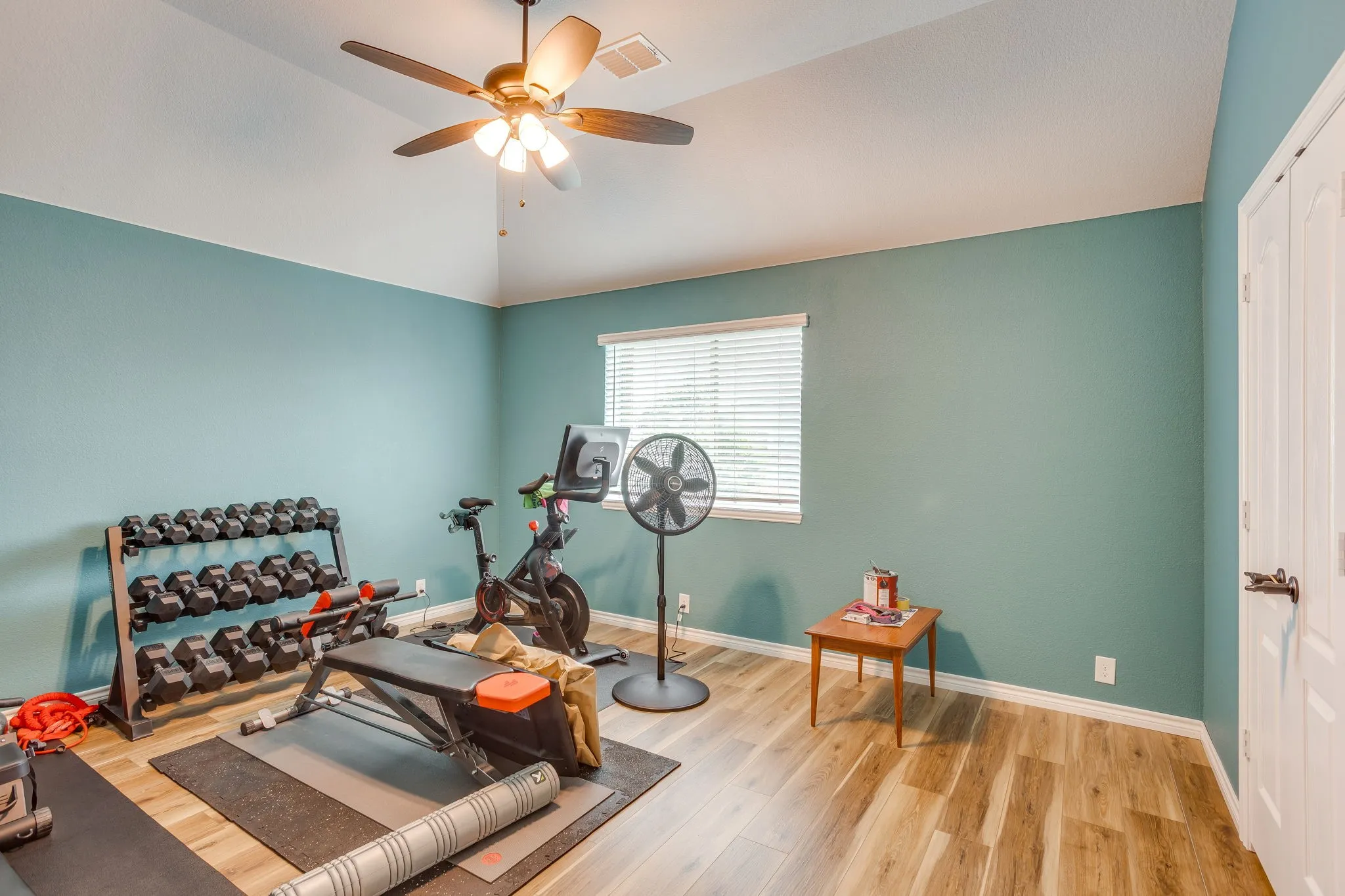 Interior room featuring vaulted ceilings, wood-finish flooring, a ceiling fan with integrated lighting, and a window with blinds