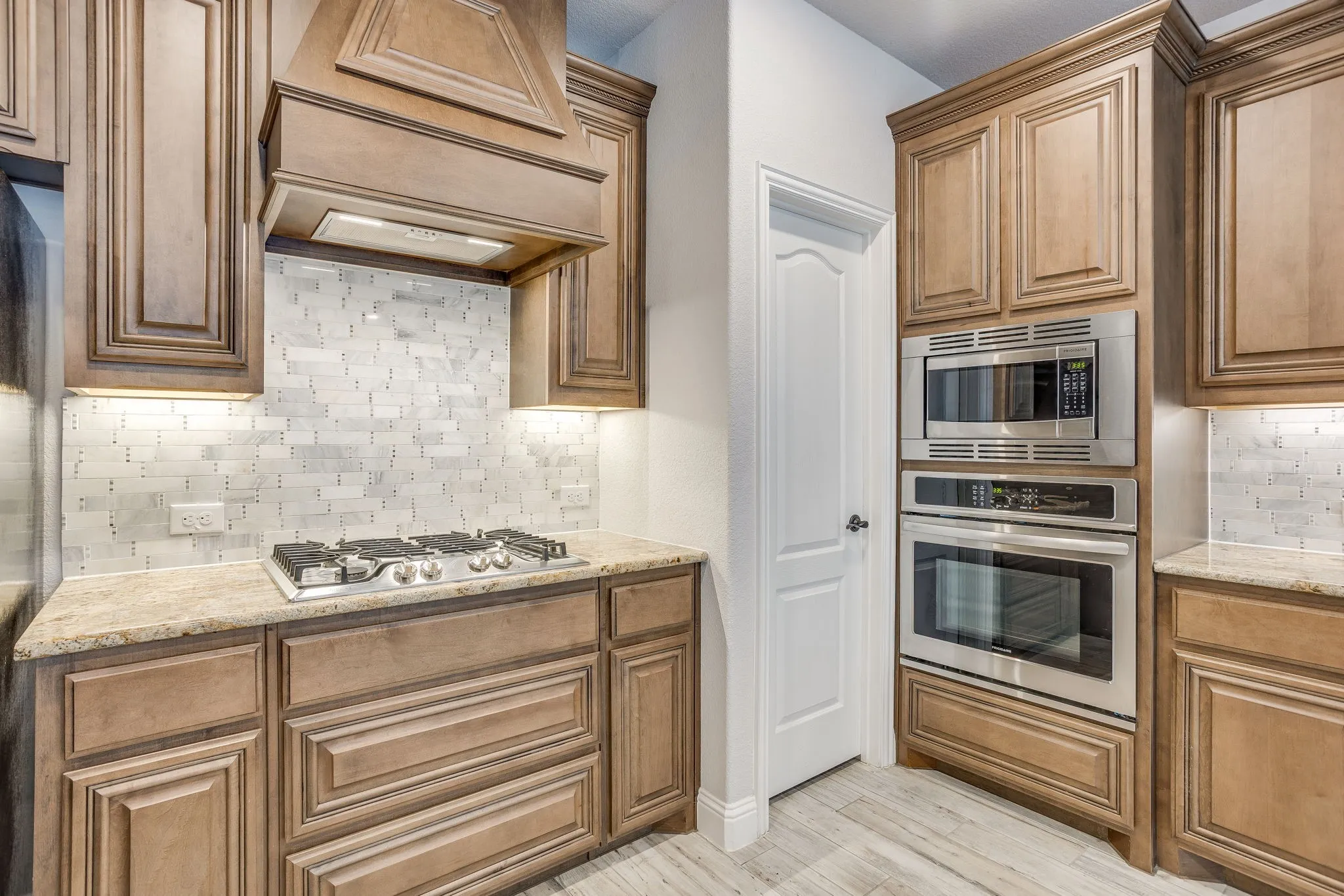 Kitchen featuring light wood-finish cabinetry, light-toned countertops, a stainless steel gas cooktop, a built-in microwave, and a built-in oven