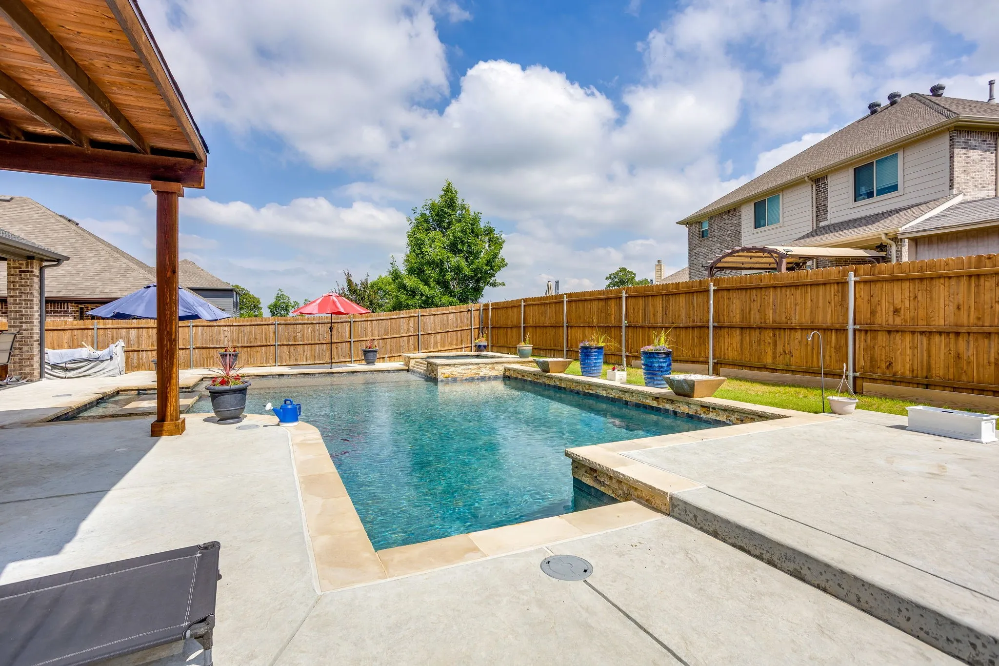 Outdoor swimming pool featuring a built-in spa, concrete patio surround, and a wooden privacy fence
