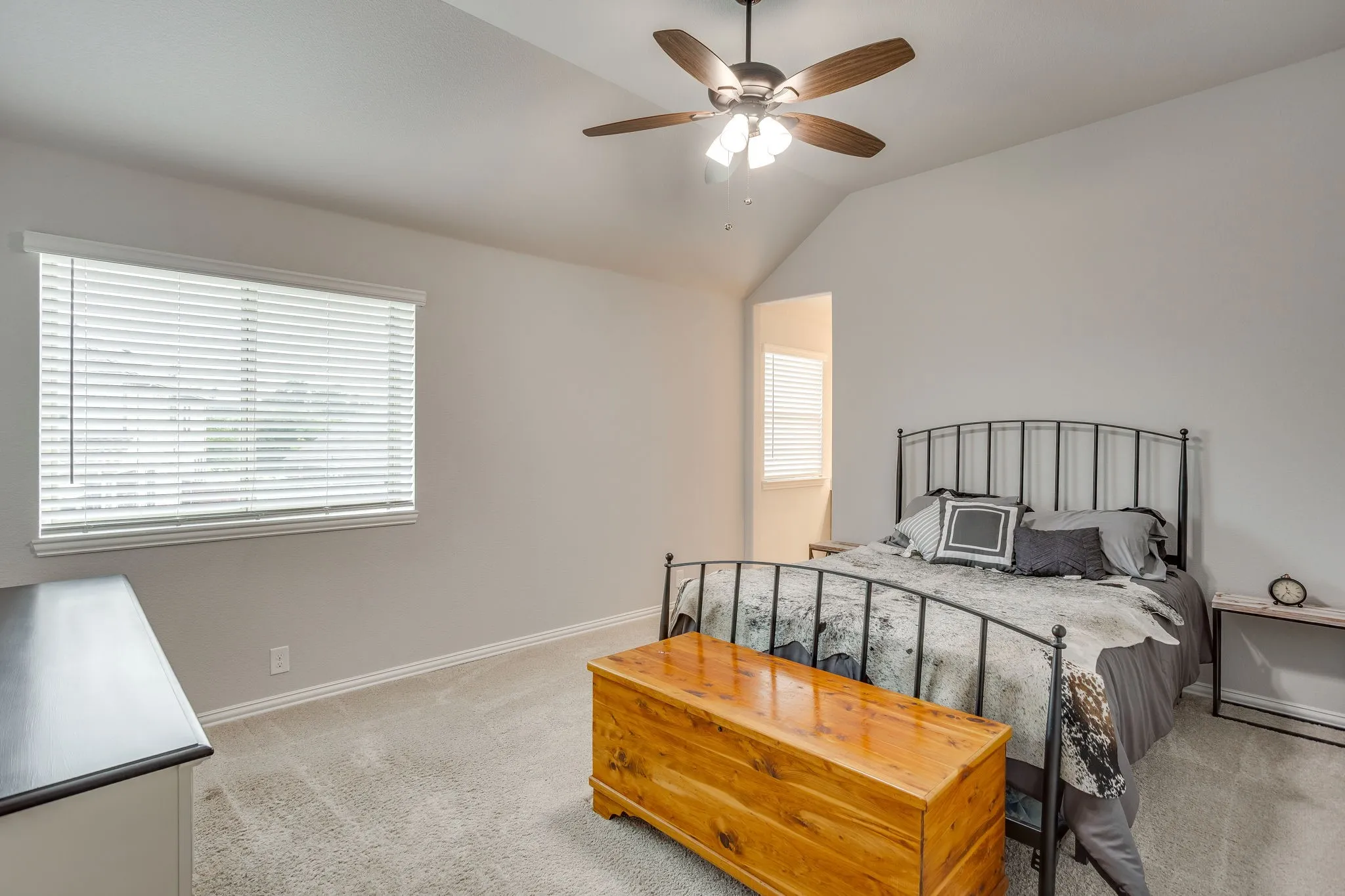 Spacious bedroom featuring vaulted ceilings, a ceiling fan with integrated lighting, window blinds for light control, and neutral-toned carpeting