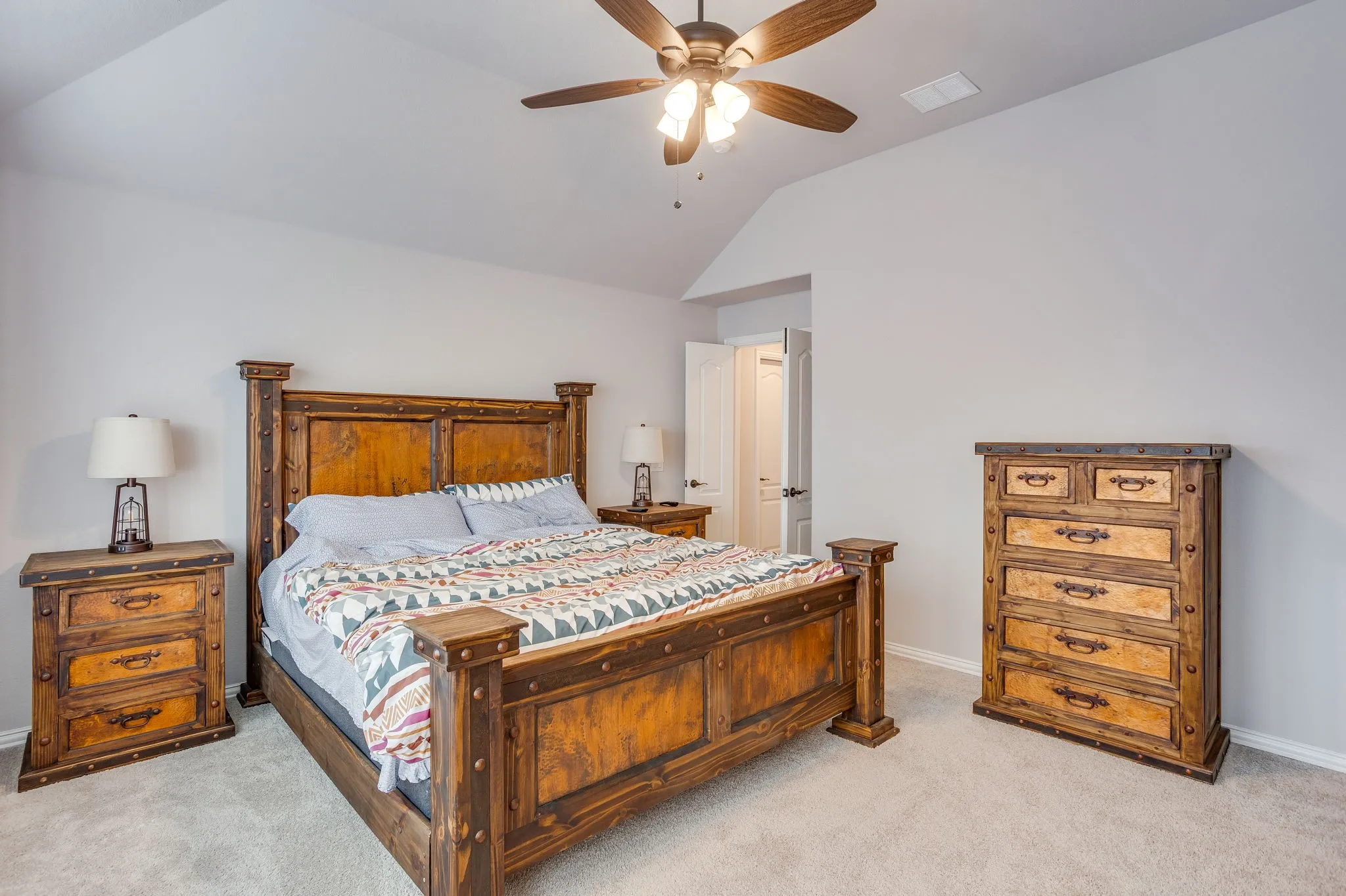 Carpeted bedroom featuring a vaulted ceiling with a ceiling fan, light gray wall paint, and a white interior door