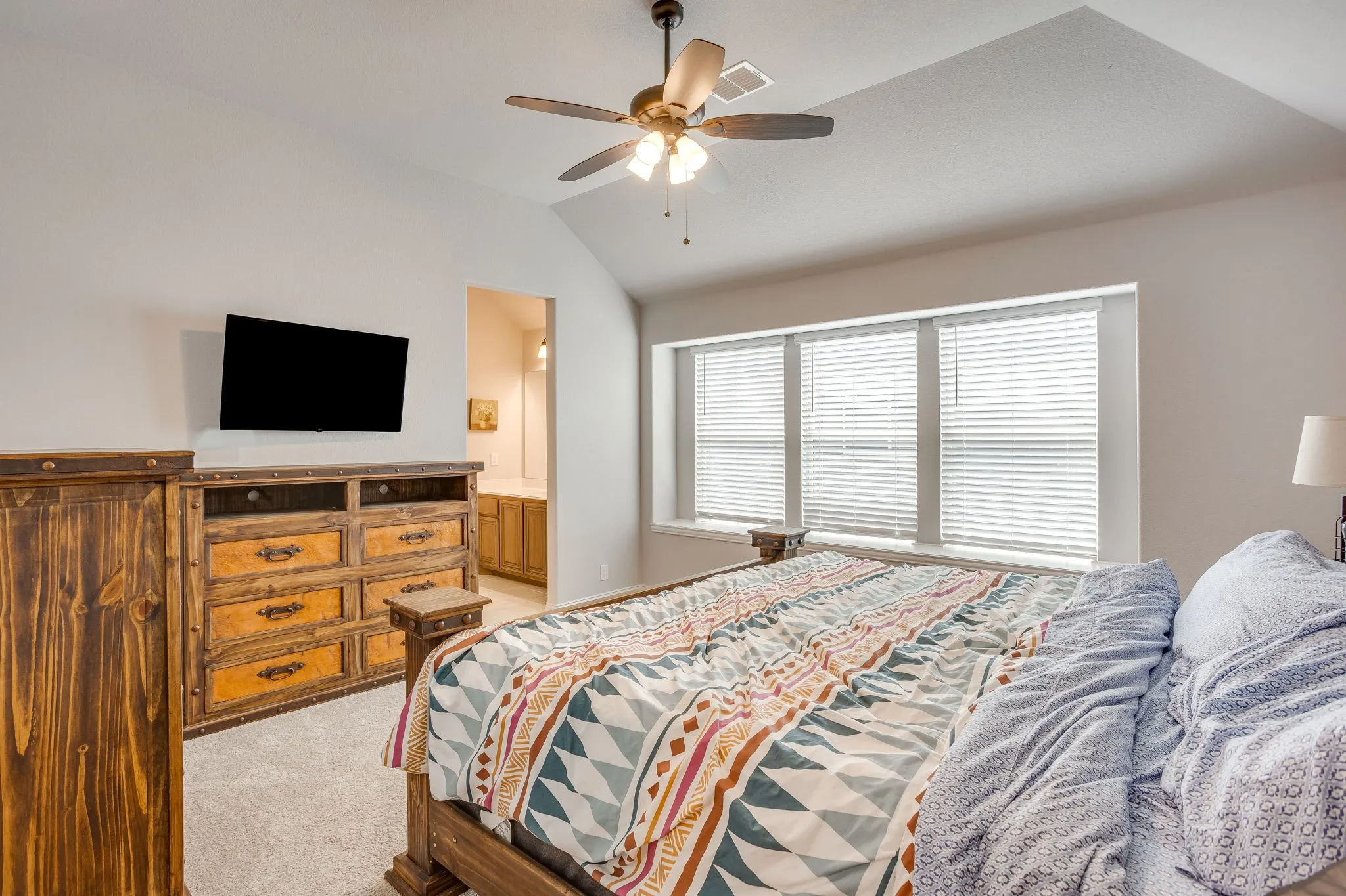 Carpeted bedroom featuring a vaulted ceiling, ceiling fan, and multiple windows with blinds