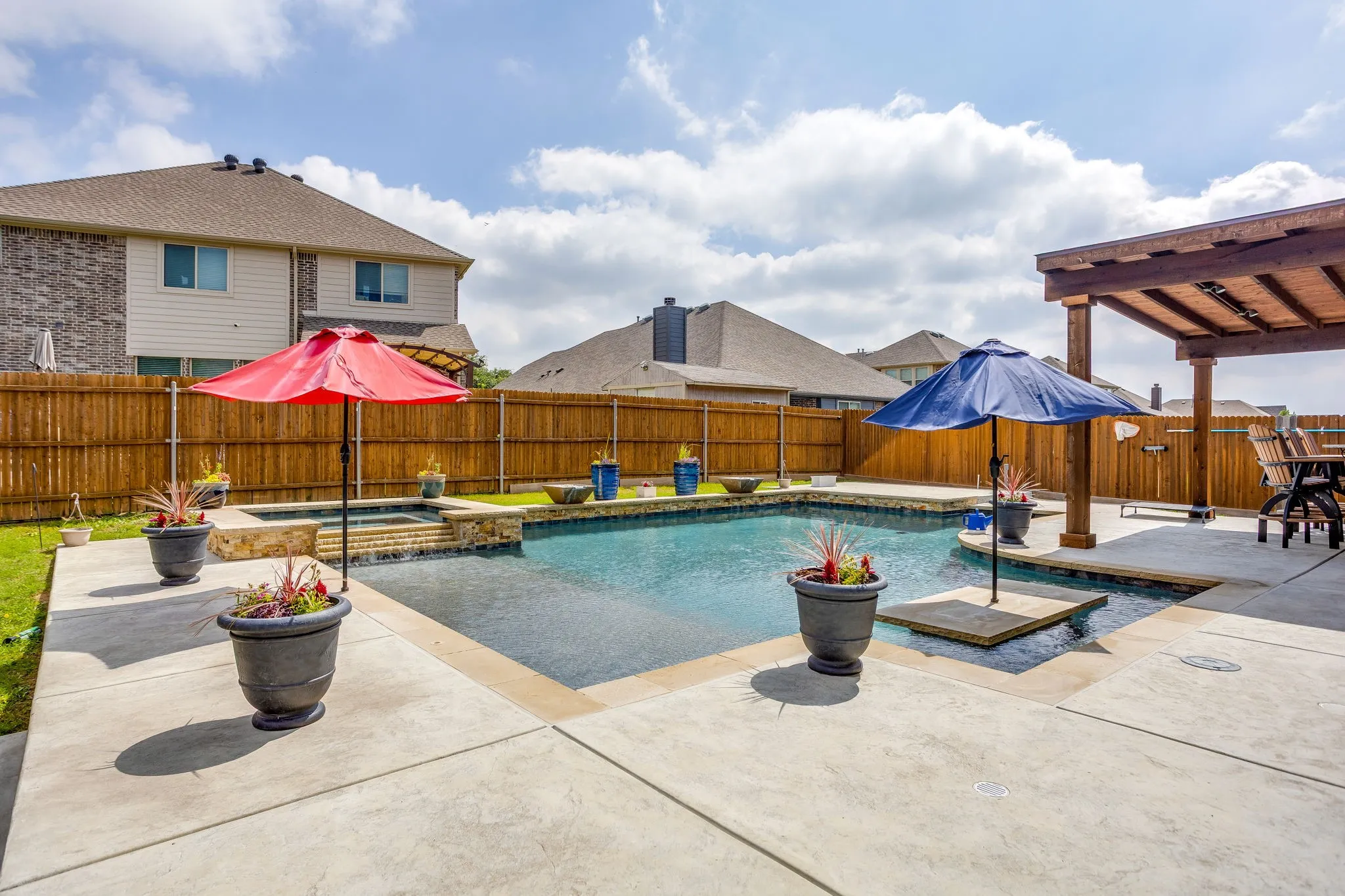 Expansive backyard featuring a built-in swimming pool with an integrated spa, concrete patio, and a wooden privacy fence