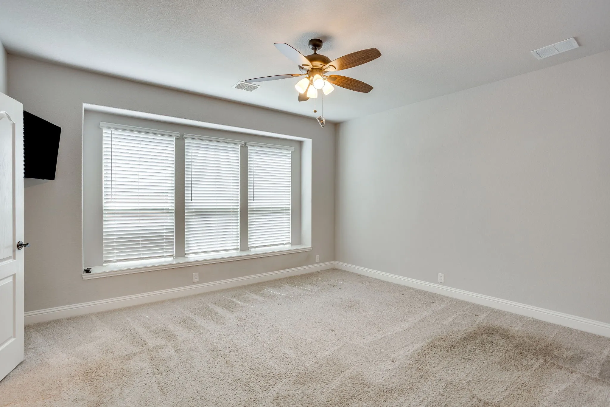 Spacious room featuring neutral carpeting, a triple window with blinds, and a ceiling fan with integrated lighting