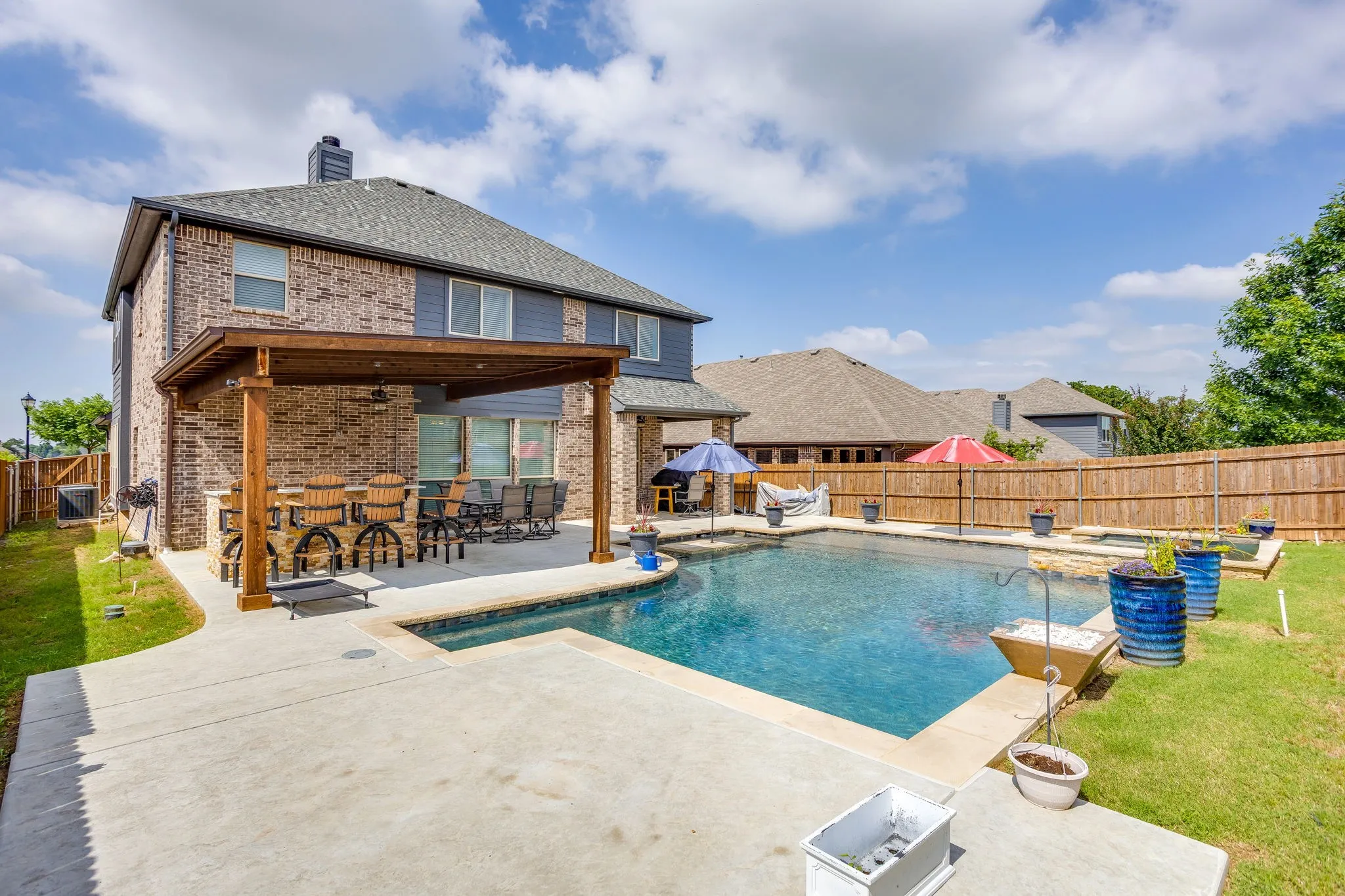 Expansive backyard featuring a rectangular swimming pool with a spa, a large covered patio, a built-in outdoor kitchen with bar seating, and a privacy fence