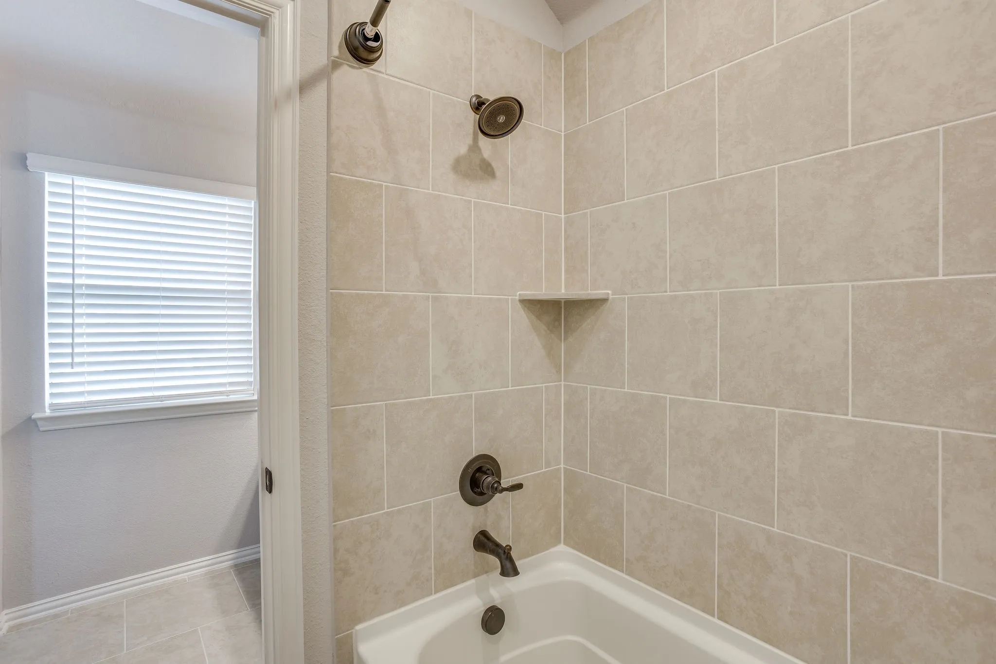 Bathtub and shower combination featuring neutral-toned subway tile surround, oil-rubbed bronze fixtures, and an integrated corner shelf
