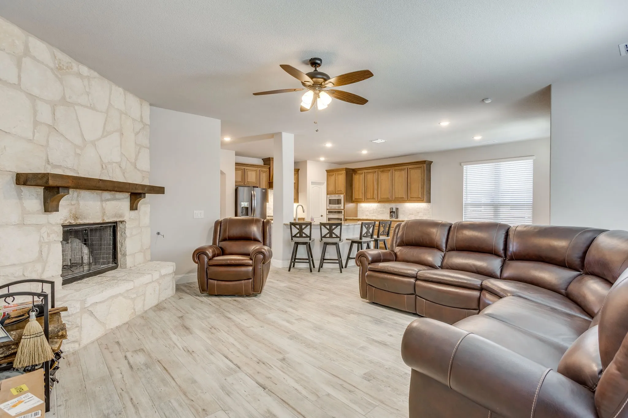 Living area featuring a stone fireplace with a wood mantle, wood-finish flooring, recessed lighting, and a ceiling fan