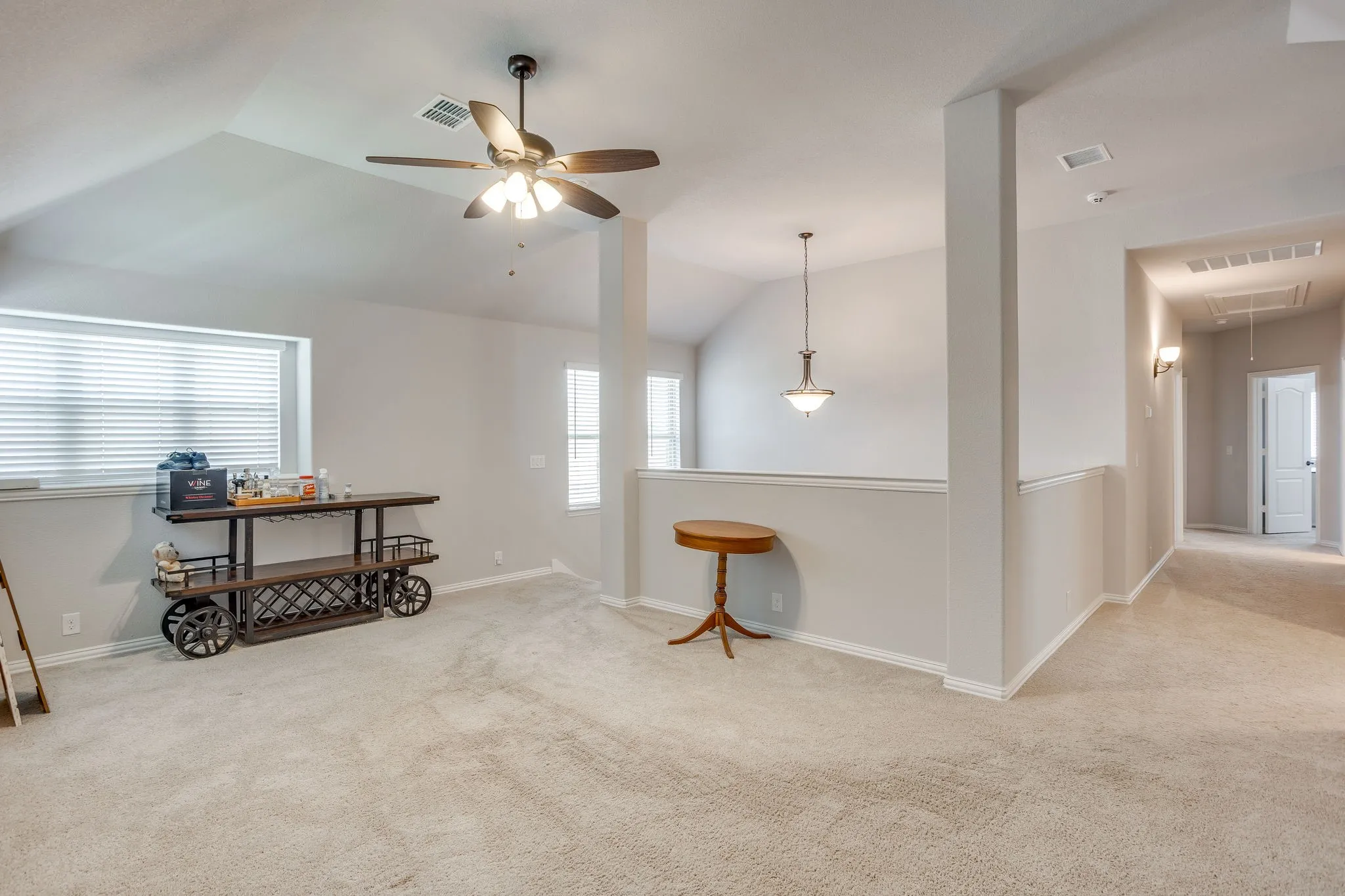 Carpeted family room featuring a vaulted ceiling with fan and contemporary pendant light over stairway.