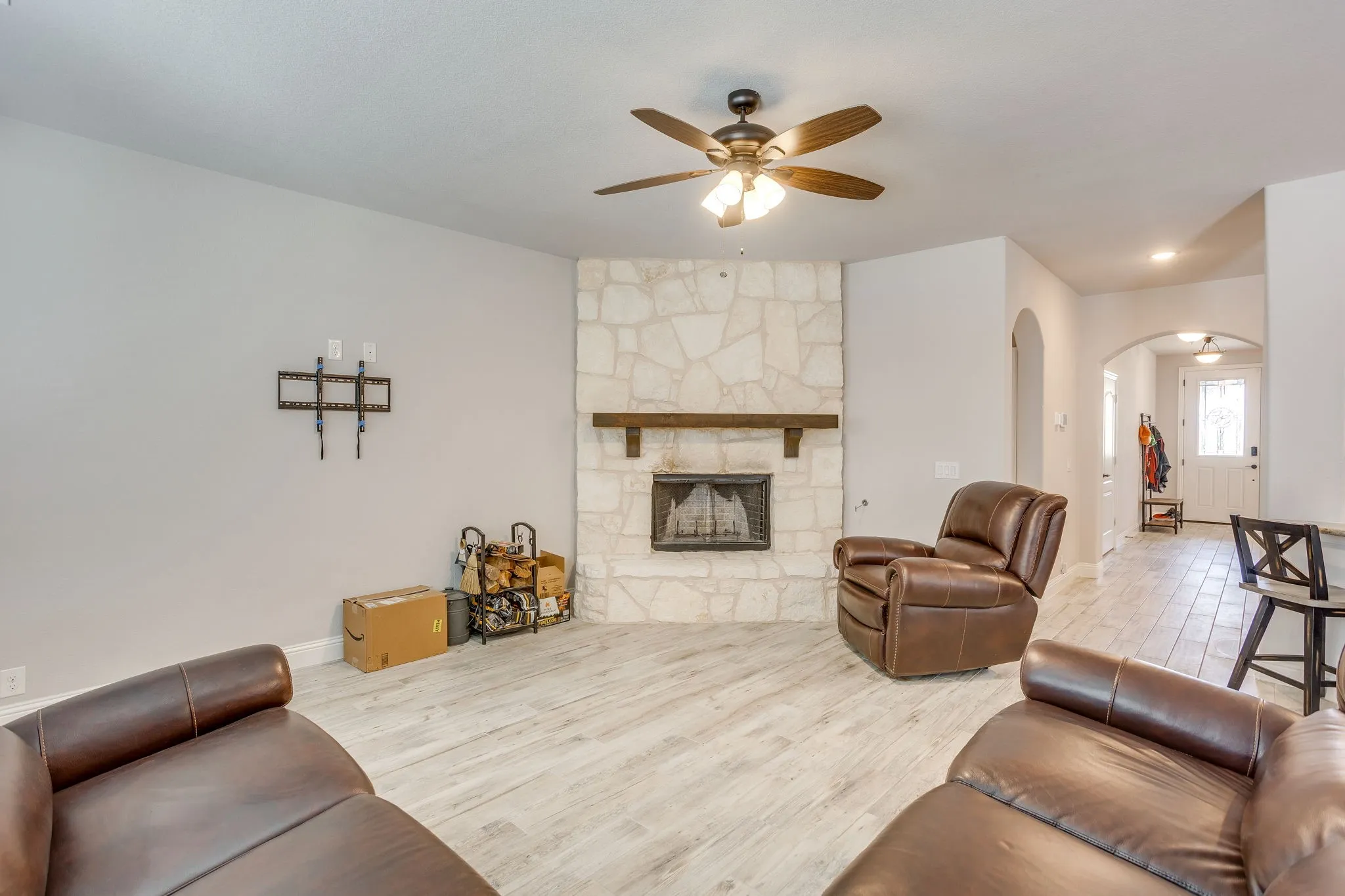 Living area featuring a stone-clad fireplace with a wood mantel, a ceiling fan with integrated lighting, and light wood-finish flooring