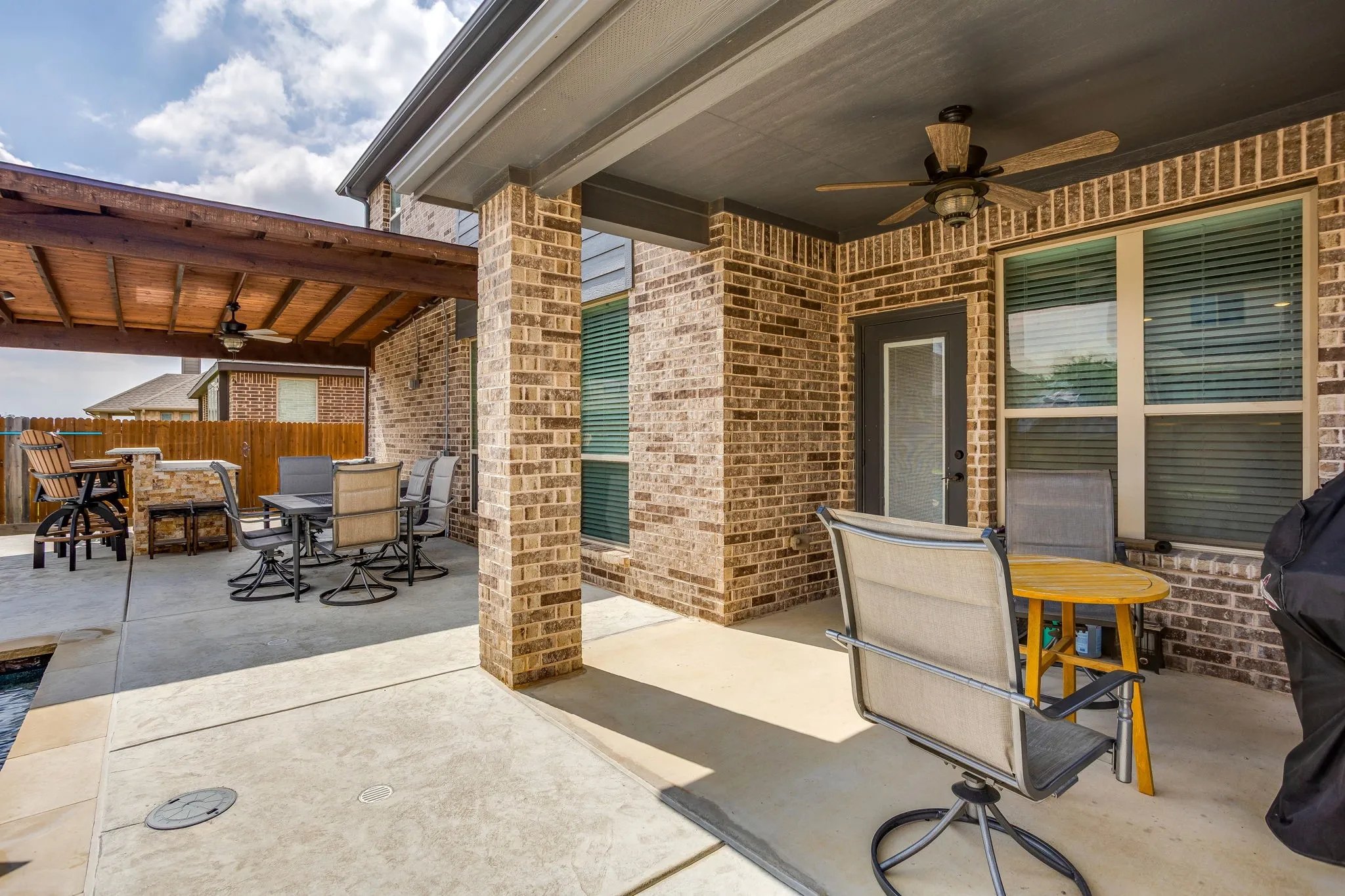 Expansive outdoor living area featuring a covered patio with brick columns, a ceiling fan, and a wood-slat pergola