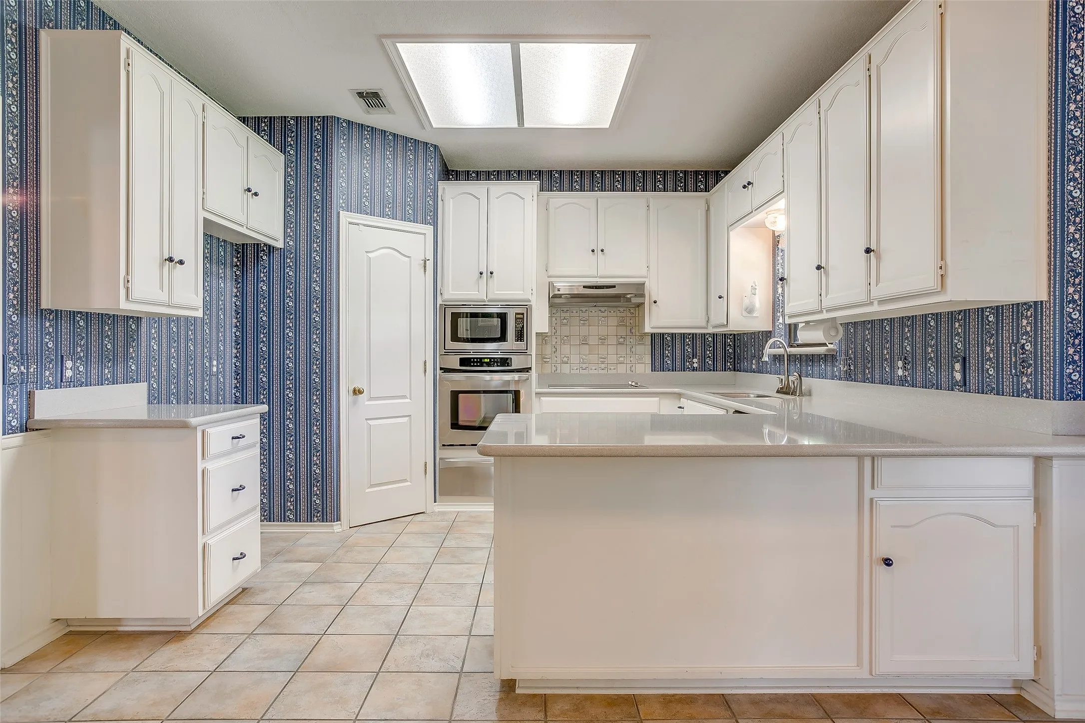 Kitchen featuring white cabinetry, light-toned countertops, built-in stainless steel appliances, a tiled backsplash, and ceramic tile flooring