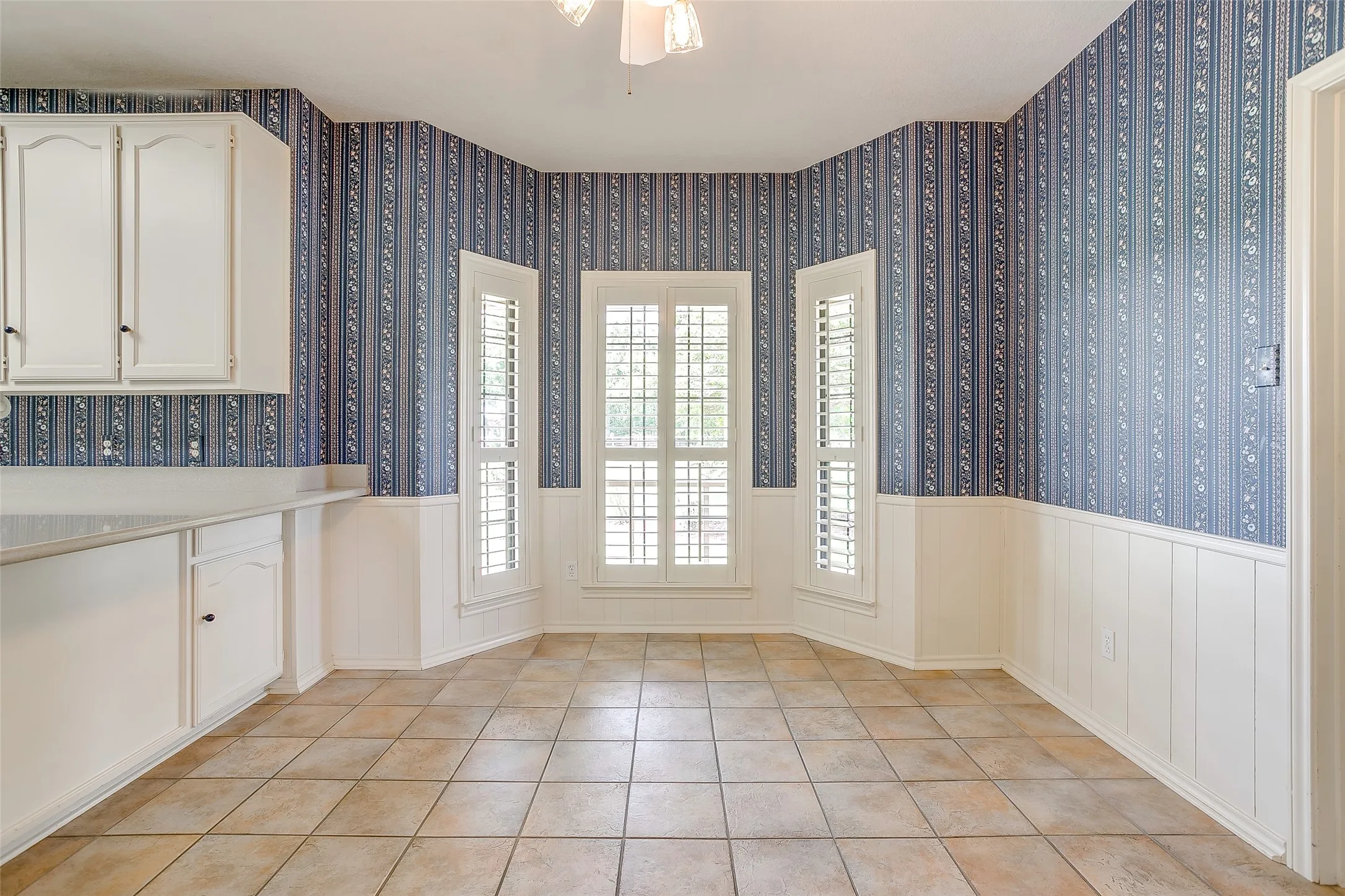 Dining area featuring a ceiling fan with integrated lighting, tiled flooring, and white wainscoting