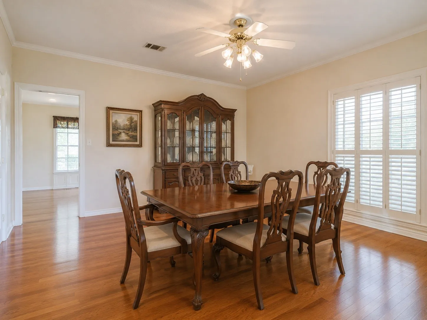 Hardwood flooring extending throughout, featuring a multi-pane window with plantation shutters and a ceiling fan with integrated lighting. Virtually staged photo.