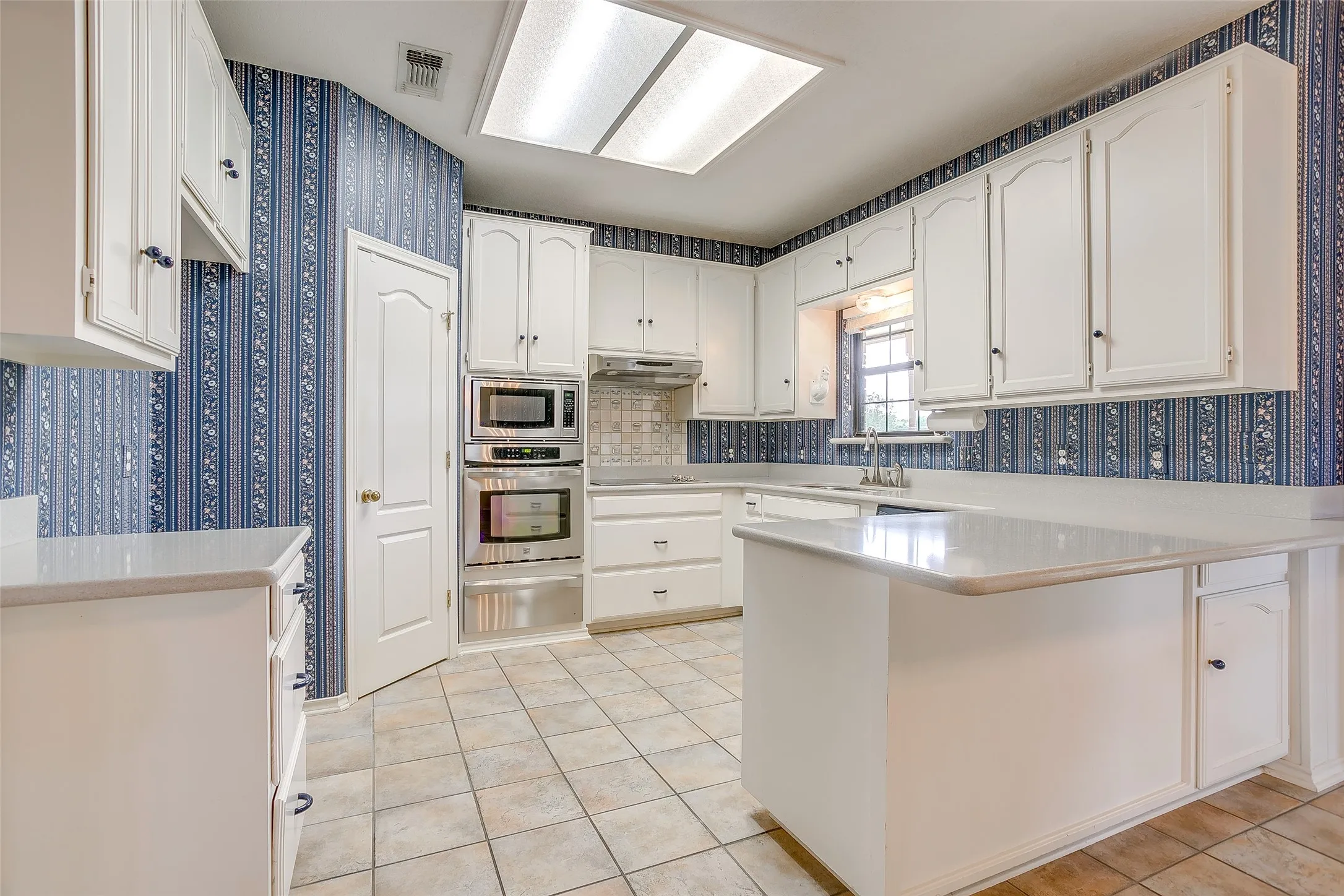 Kitchen featuring white cabinetry with dark hardware, a center island with countertop seating, tiled flooring, built-in stainless steel appliances, and a window above the sink