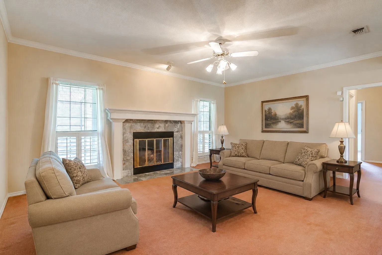 Virtually staged living room. Living room featuring a central fireplace with stone surround and mantle, a ceiling fan, and crown molding