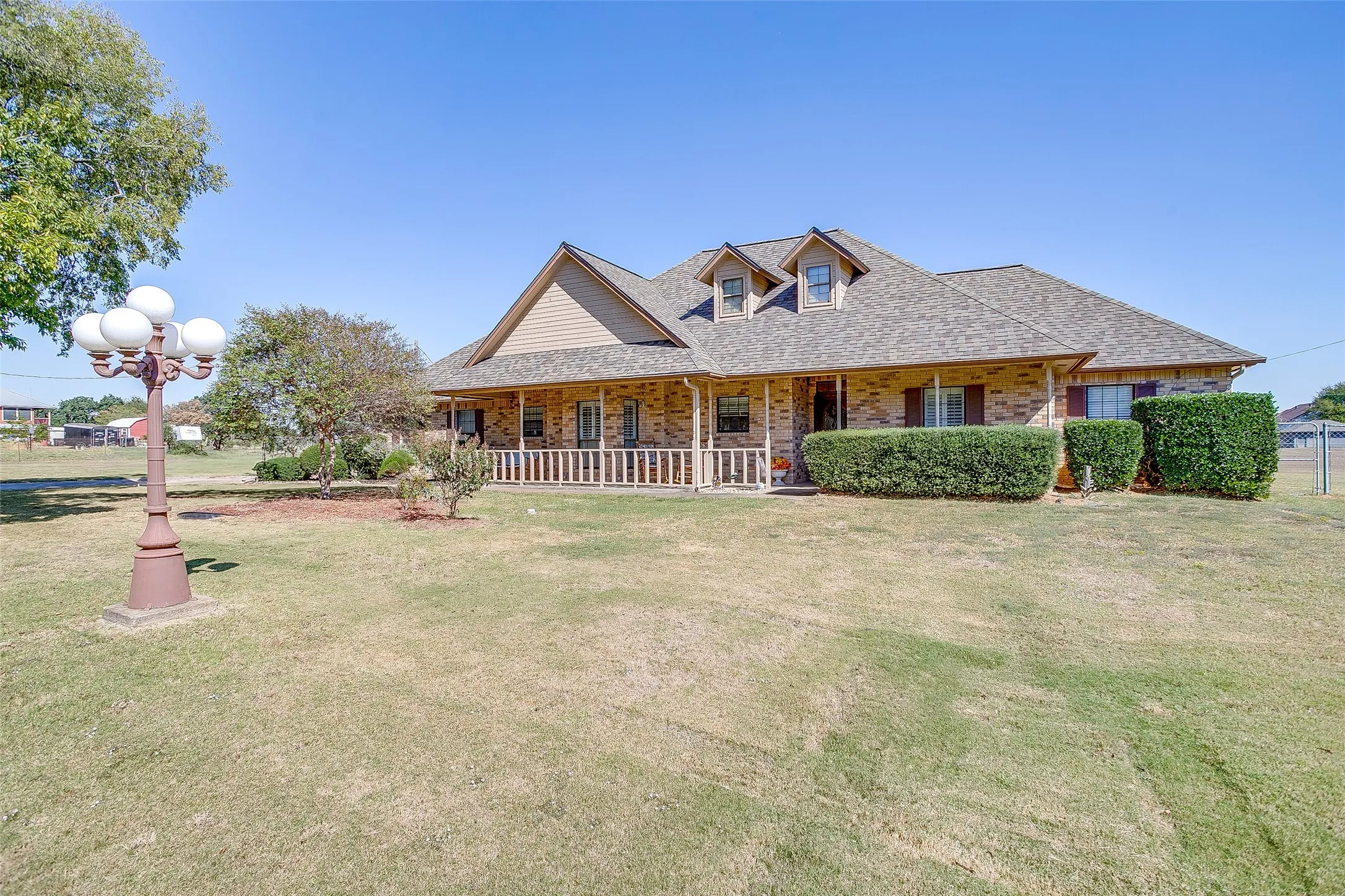 Brick exterior home featuring a covered front porch with white railing, dormer windows, and dark brown window shutters