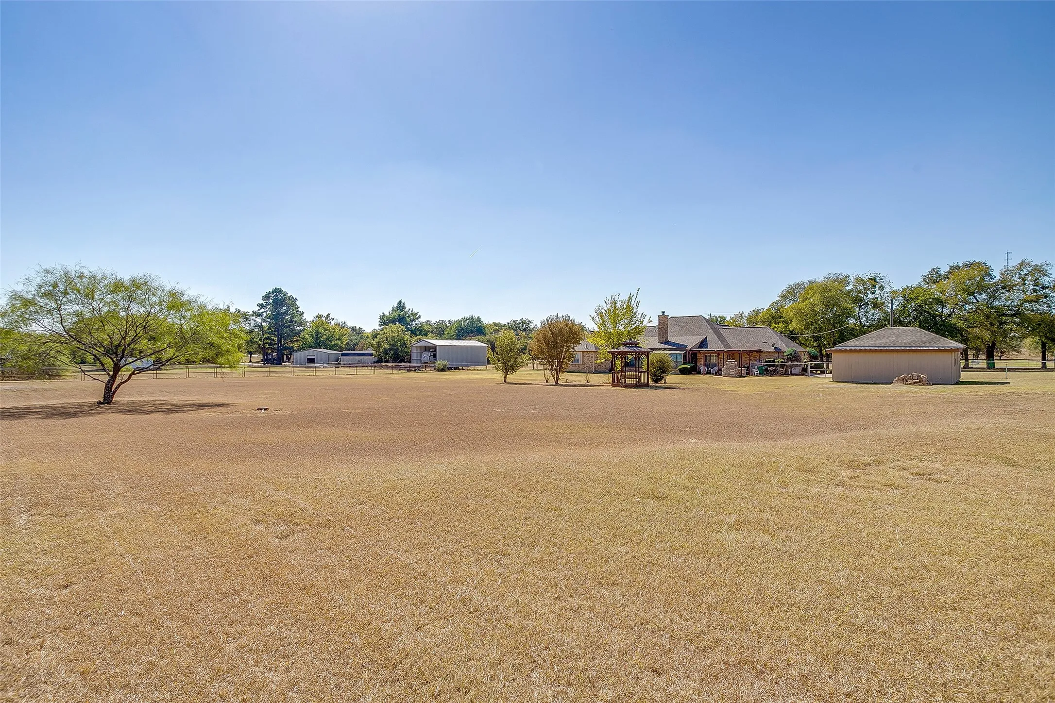 Expansive open yard with a large main residence, detached garage, and multiple outbuildings