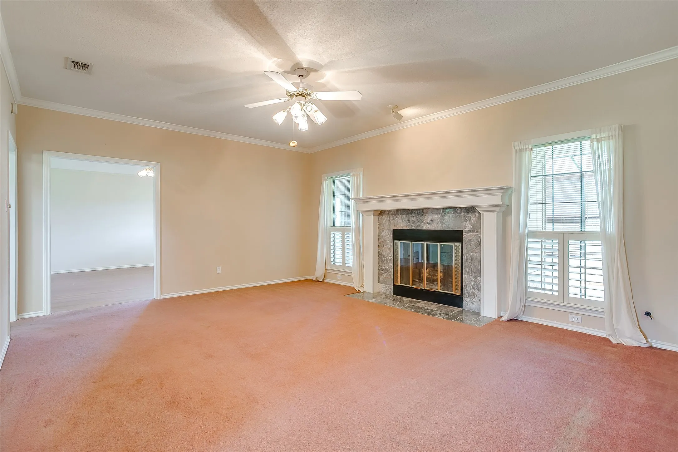 Spacious living area featuring a central fireplace with a stone surround and white mantel, crown molding, and a ceiling fan