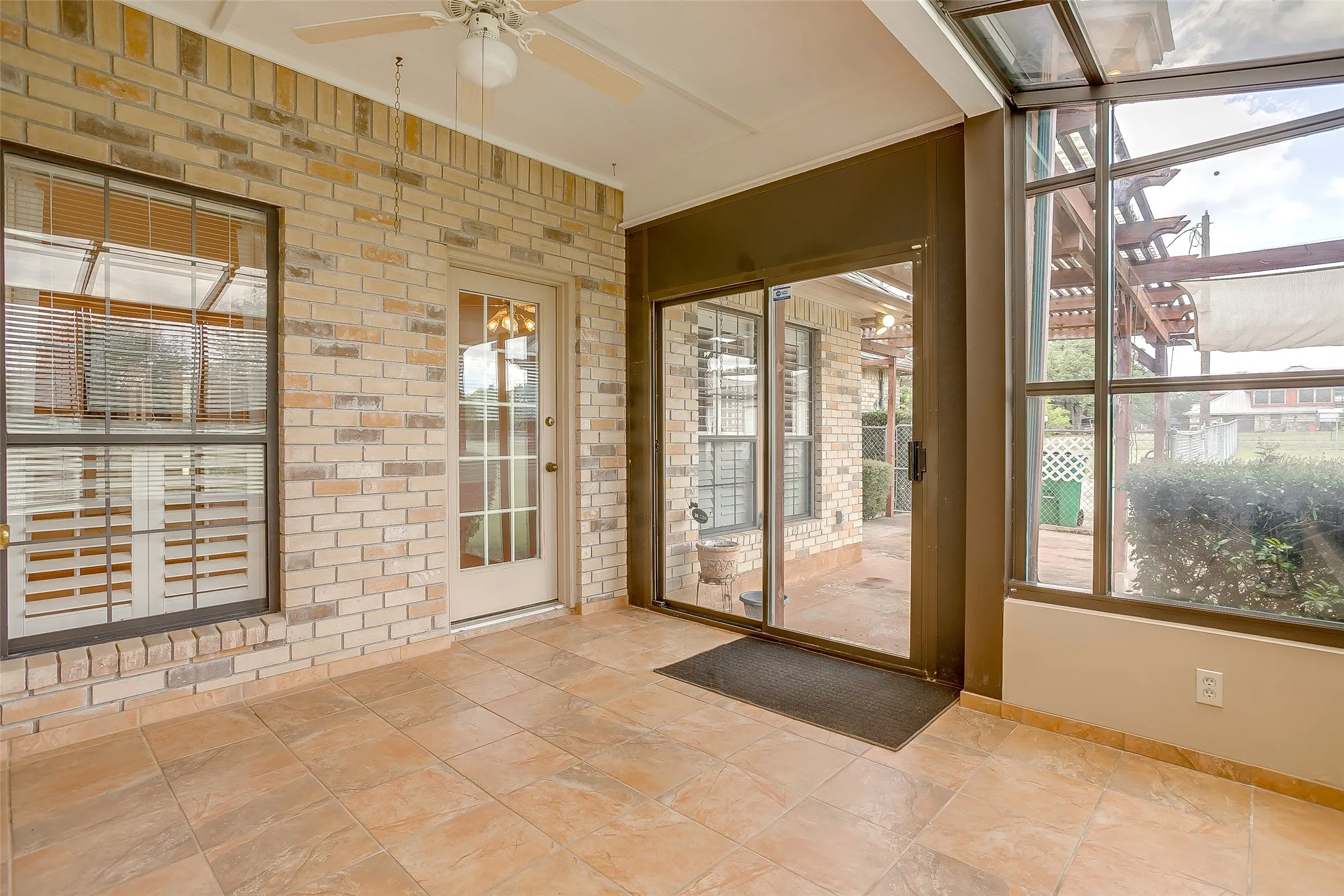 Enclosed patio featuring light-toned brick walls, large format tile flooring, and a ceiling fan