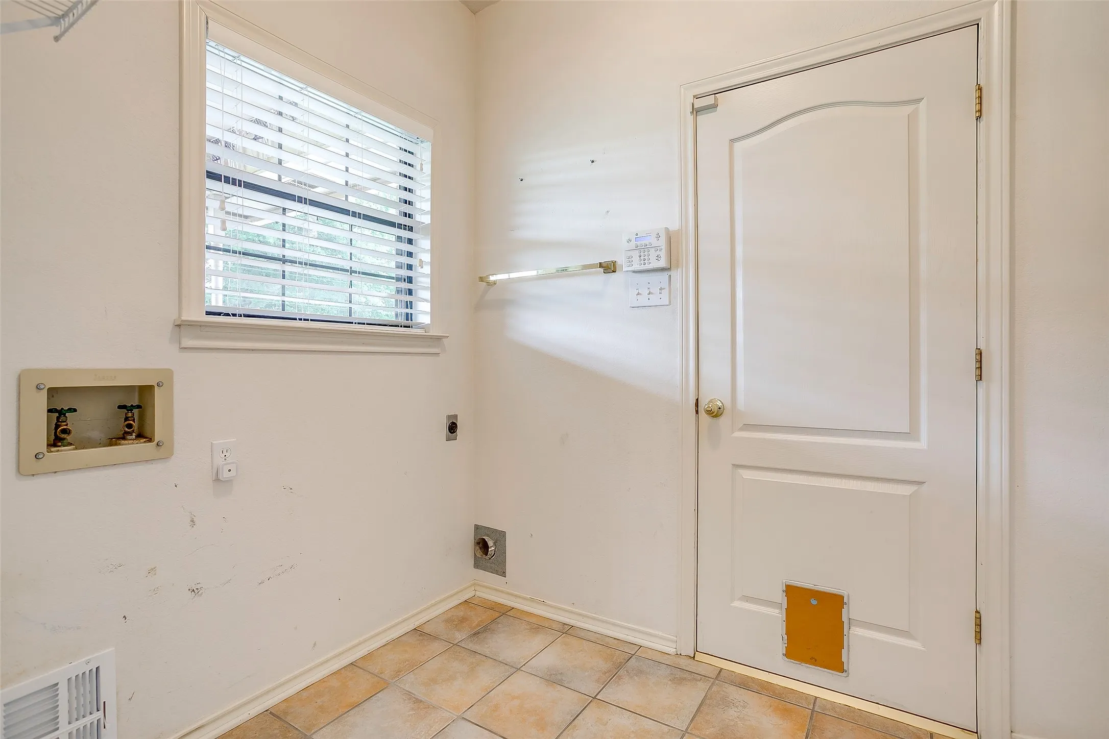 Utility area featuring a window with blinds, tile flooring, and a paneled door