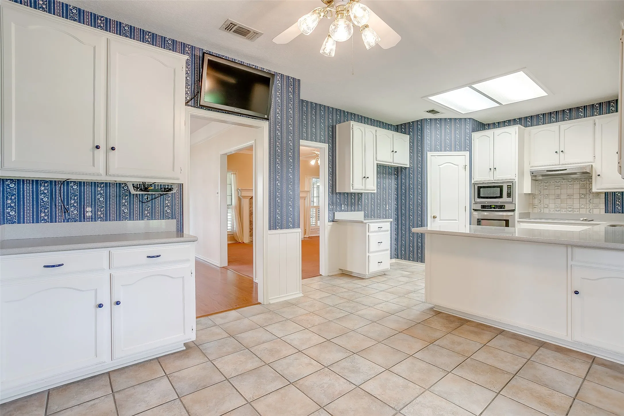 Kitchen featuring tile flooring, white cabinetry, a built-in oven and microwave, a tile backsplash, and a ceiling-mounted skylight