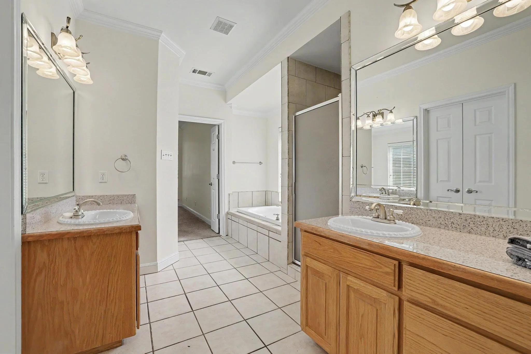 Bathroom featuring a dual vanity with light wood cabinetry, a built-in jetted tub, and a shower enclosure.