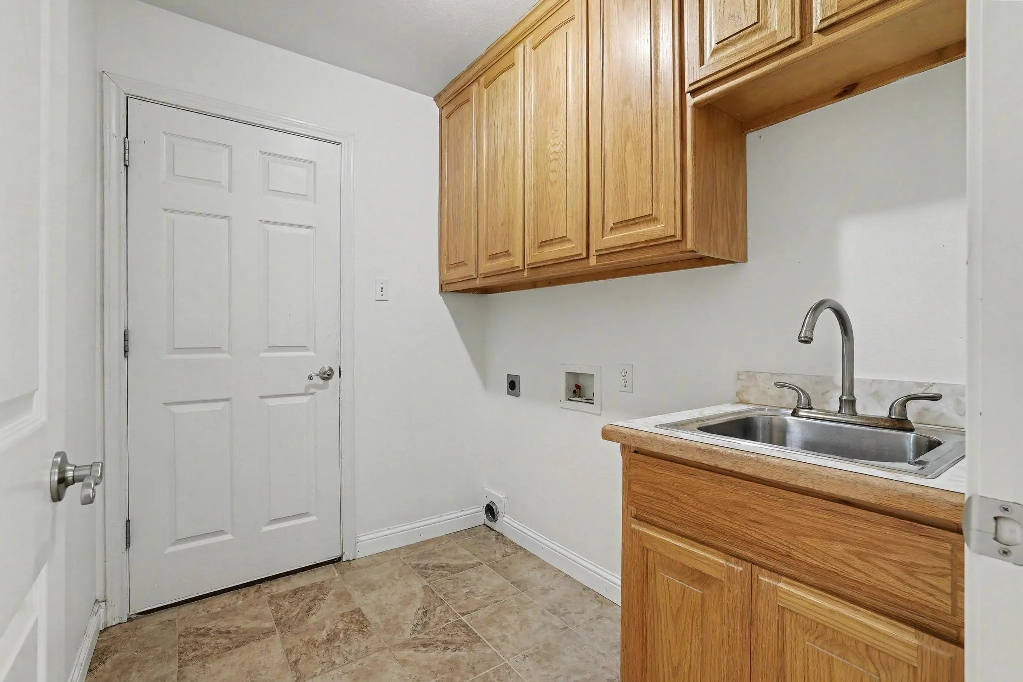 Laundry room featuring a utility sink, light wood cabinetry, and tiled flooring.