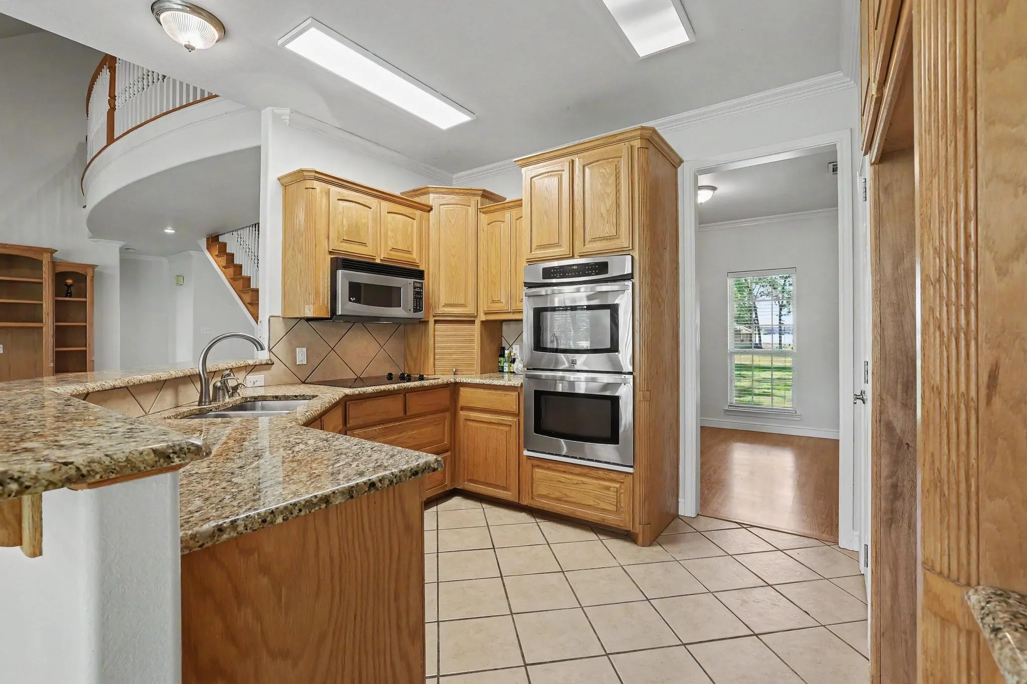 Kitchen featuring light wood cabinetry, stainless steel double ovens, and granite countertops, and a walk-in pantry.