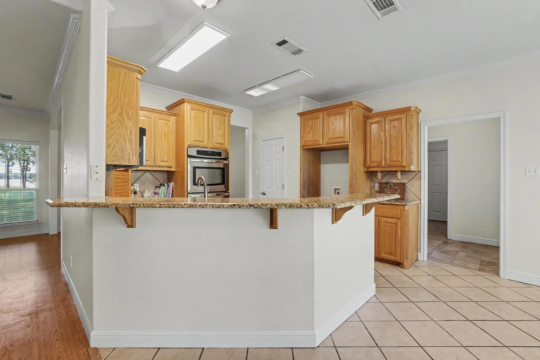 Kitchen featuring light wood cabinetry, stainless steel built-in double oven, granite countertops, and tile backsplash.