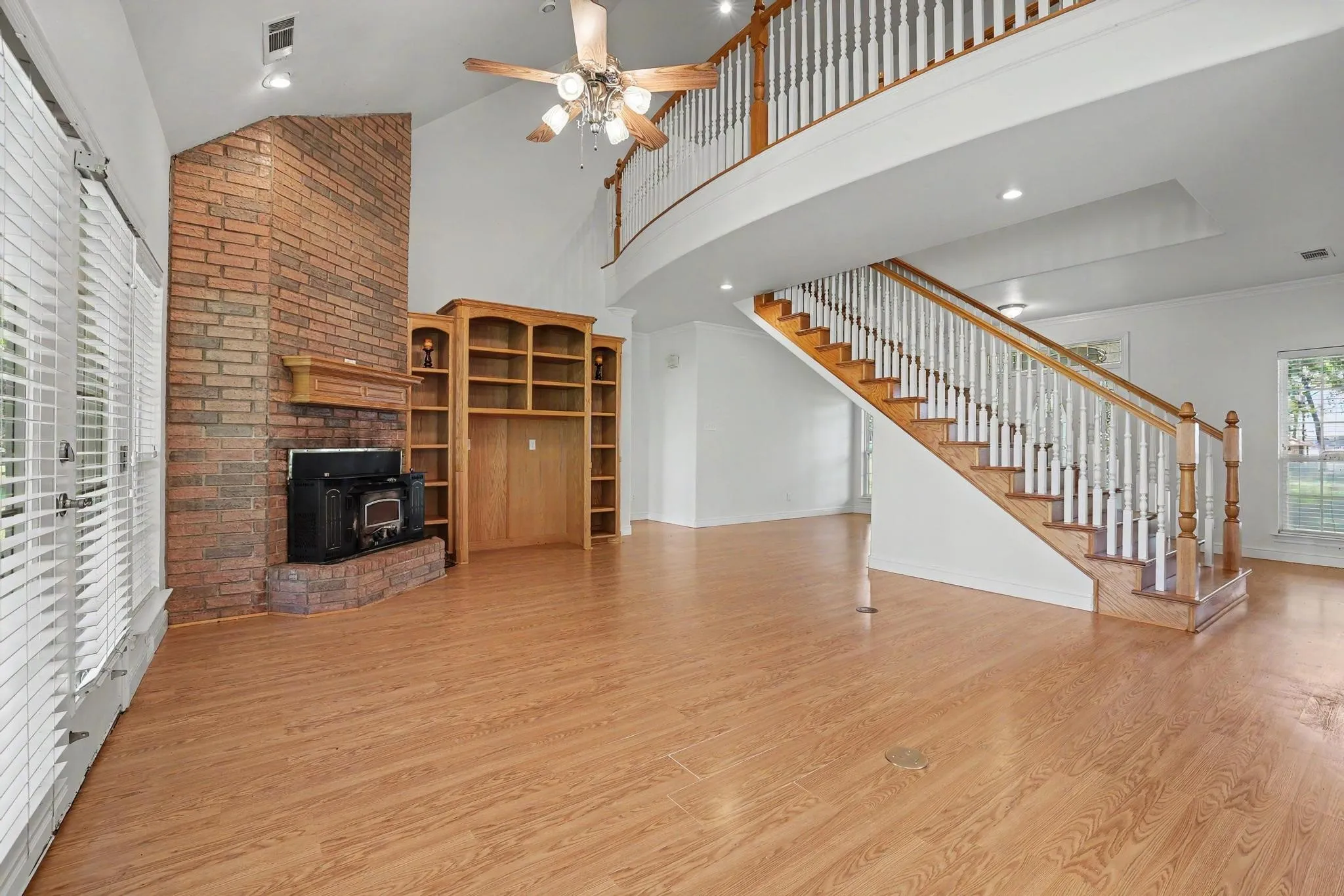 Open-concept living area featuring wood-finish flooring, a brick fireplace with a wood-burning insert, and built-in shelving.