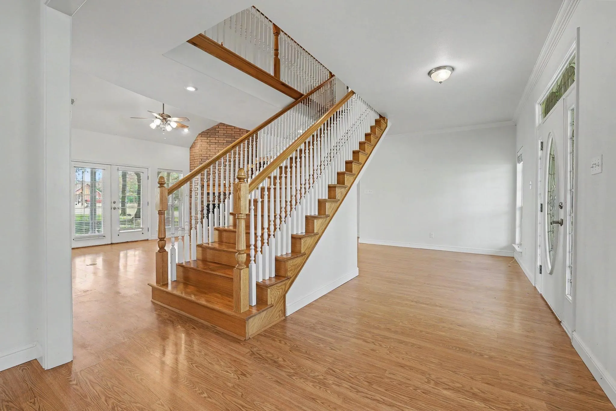 Inviting entryway featuring wood-finish flooring, a grand staircase with wood banisters and white spindles, and a white paneled front door with decorative glass inserts.