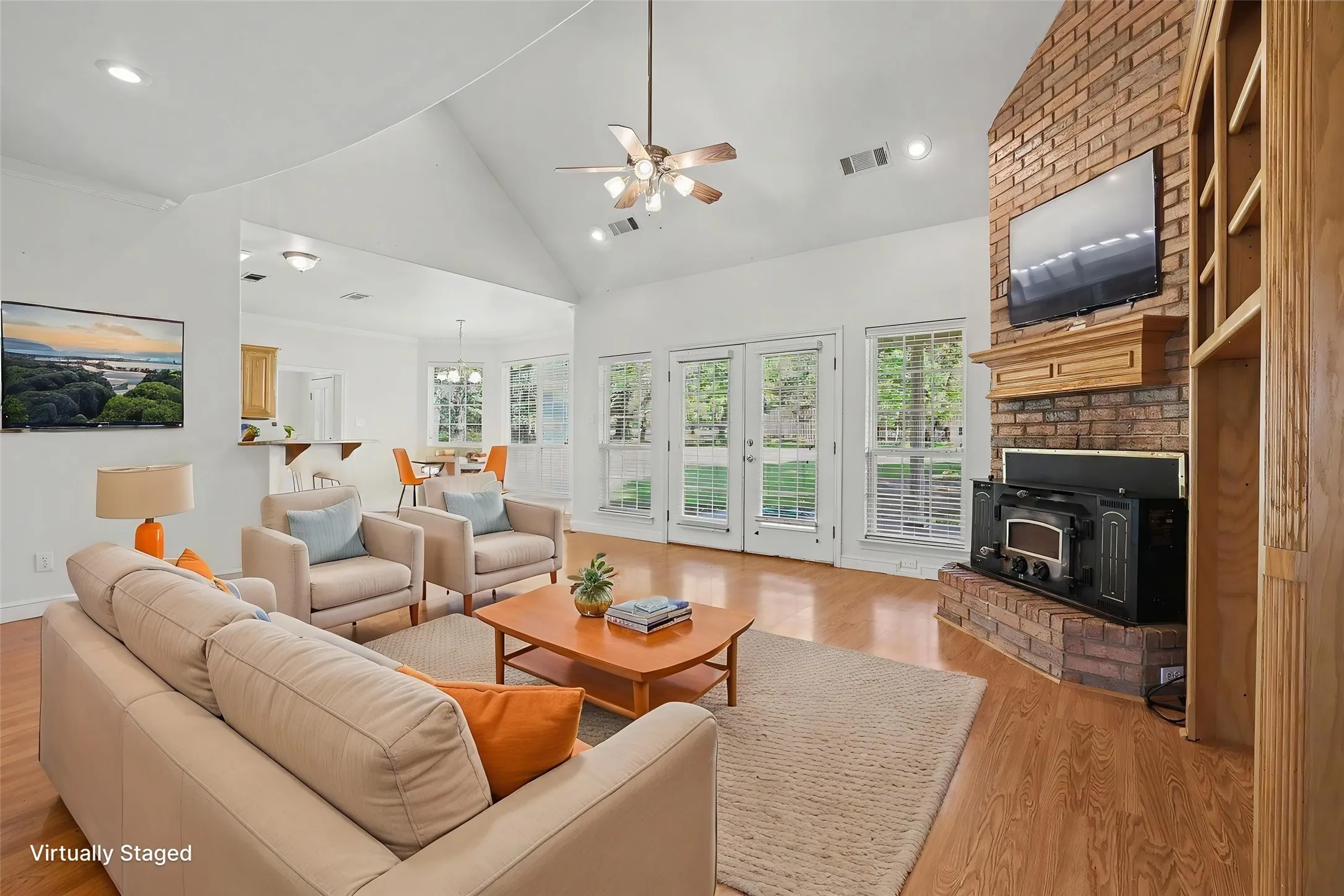 Vaulted ceiling living room featuring wood-finish flooring, a brick fireplace with a wood-burning insert, and built-in shelving.