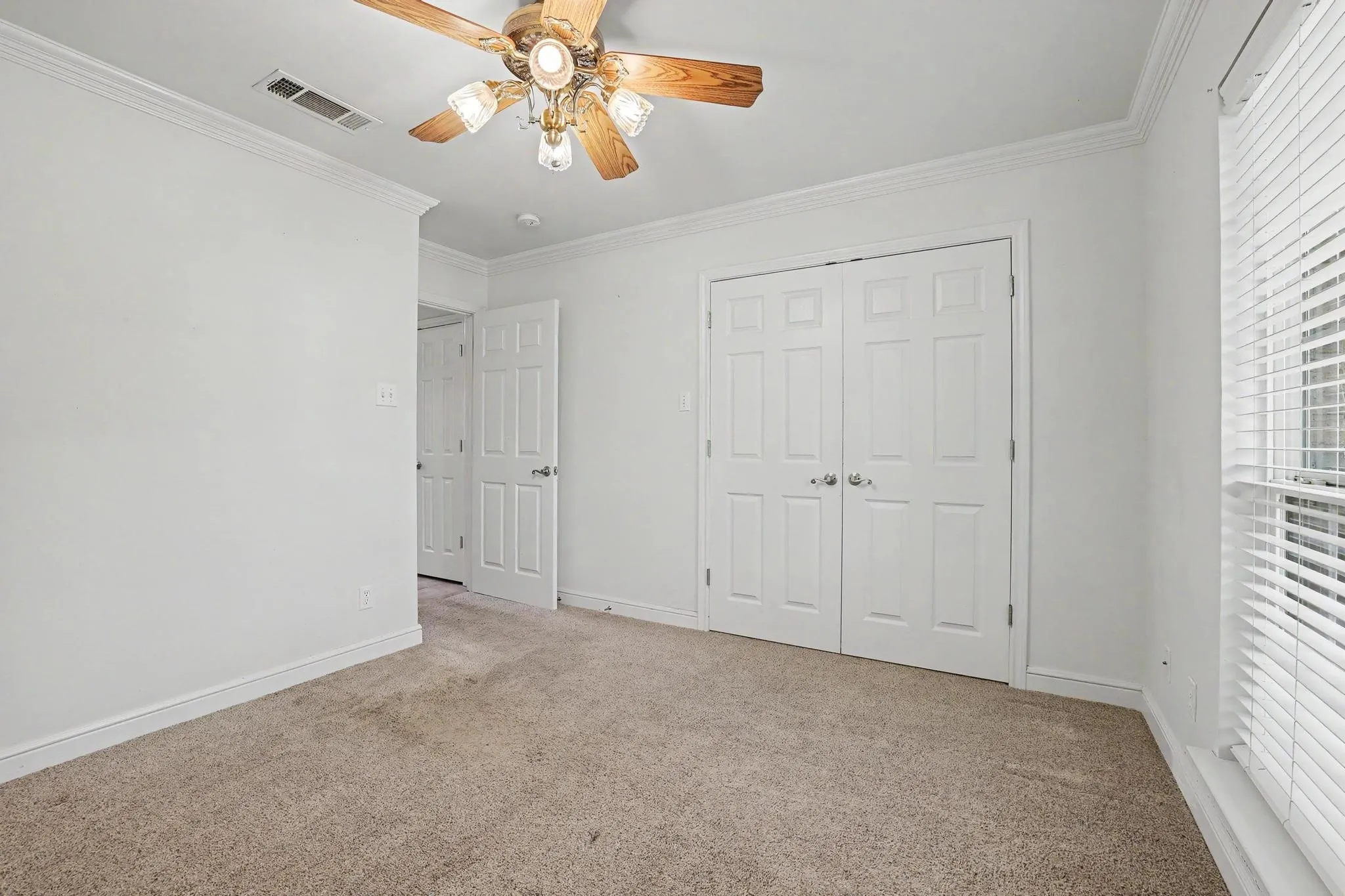 Another view of the downstairs secondary bedroom with white walls, crown molding, and white baseboards.