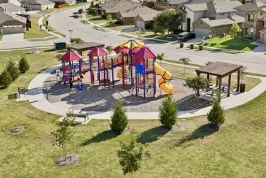 Community park featuring playground equipment with slides and climbing structures, a covered picnic area, benches, and a walking path