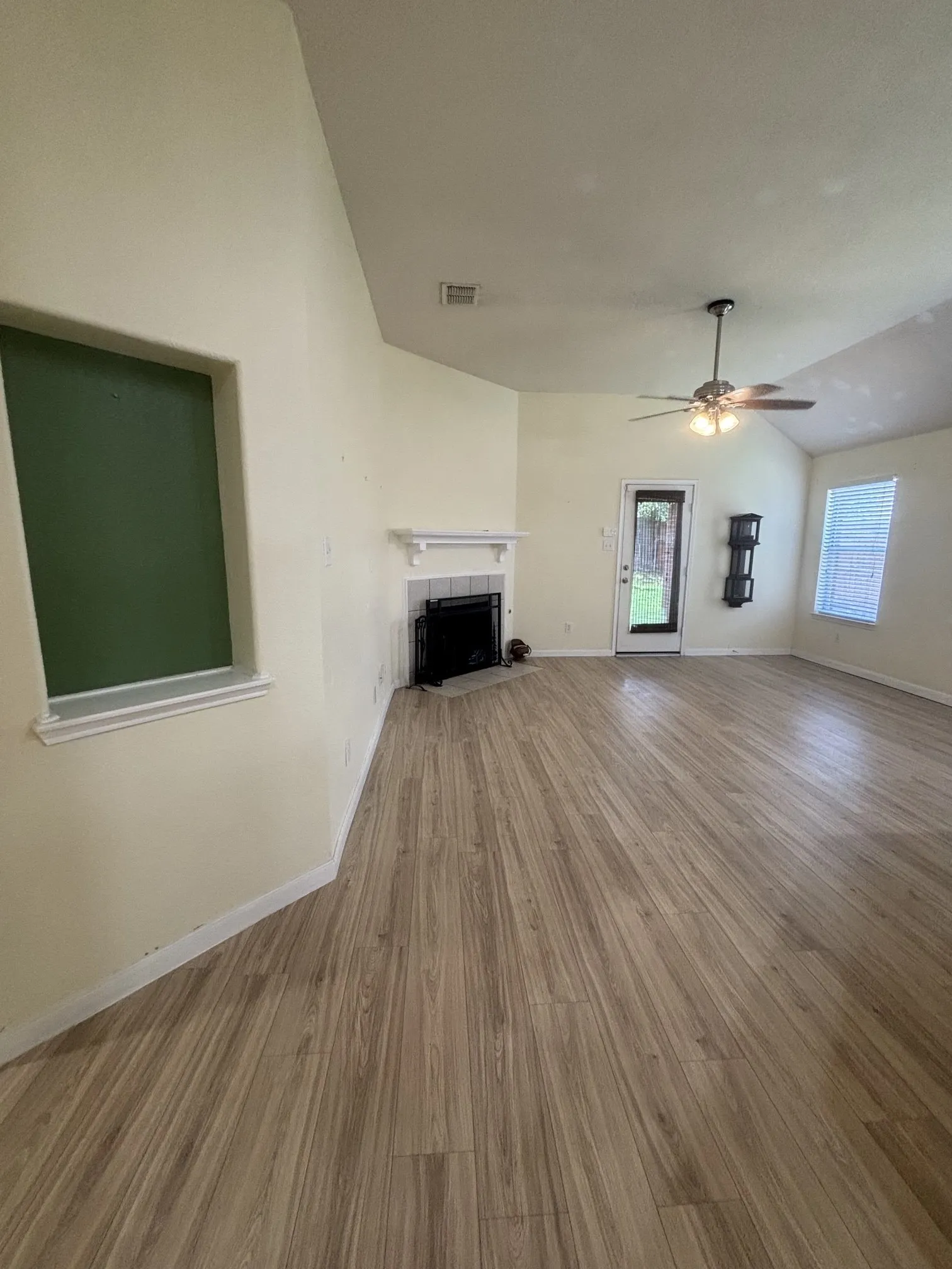 Spacious living area featuring vaulted ceilings, wood-finish flooring, and a fireplace with a white mantel