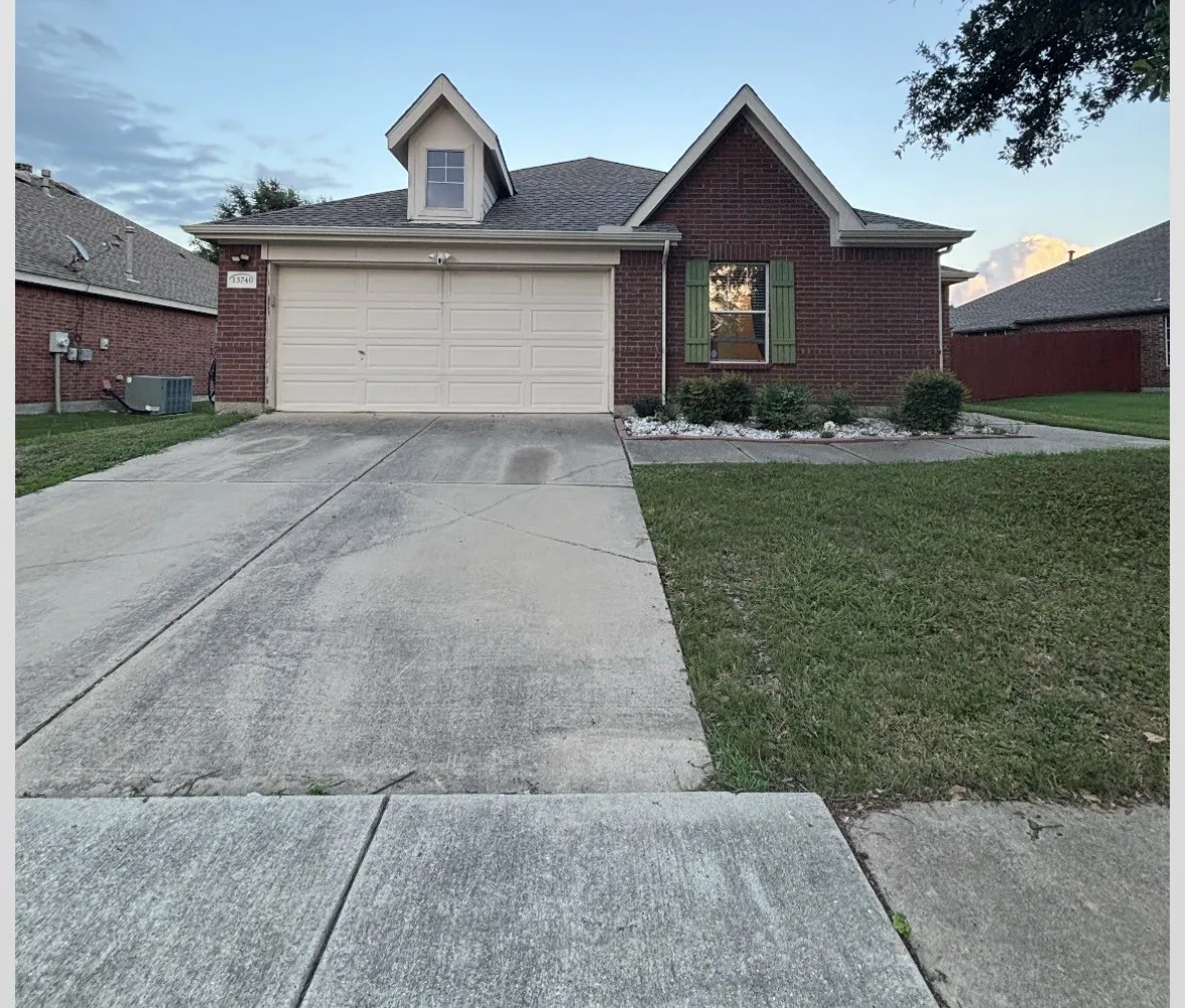 Brick exterior featuring a two-car garage, dormer window, and mature landscaping