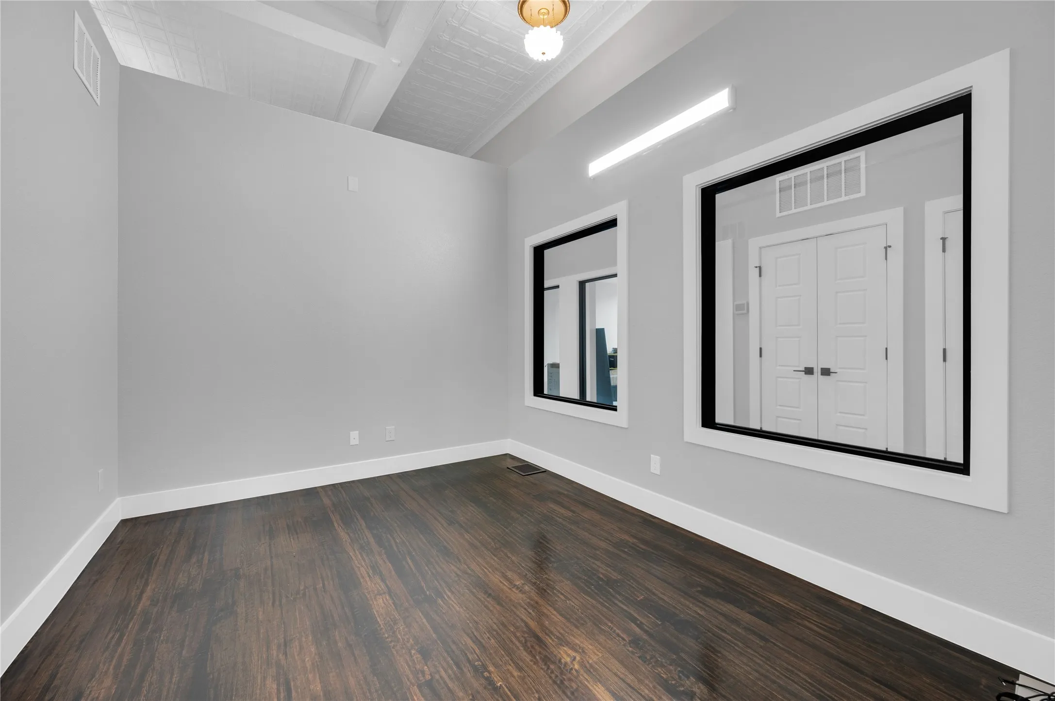 Spacious room featuring vaulted ceilings with exposed beams, wood-finish flooring, and two framed wall openings