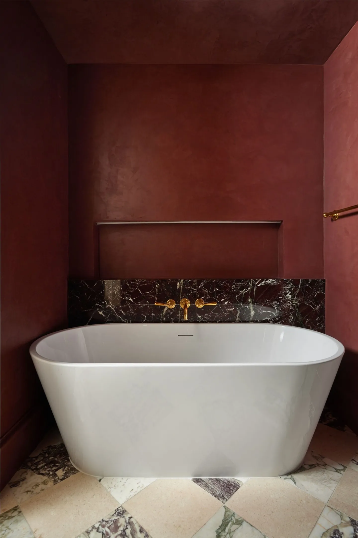 Freestanding soaking tub with dark marble surround and gold-finish wall-mounted fixtures