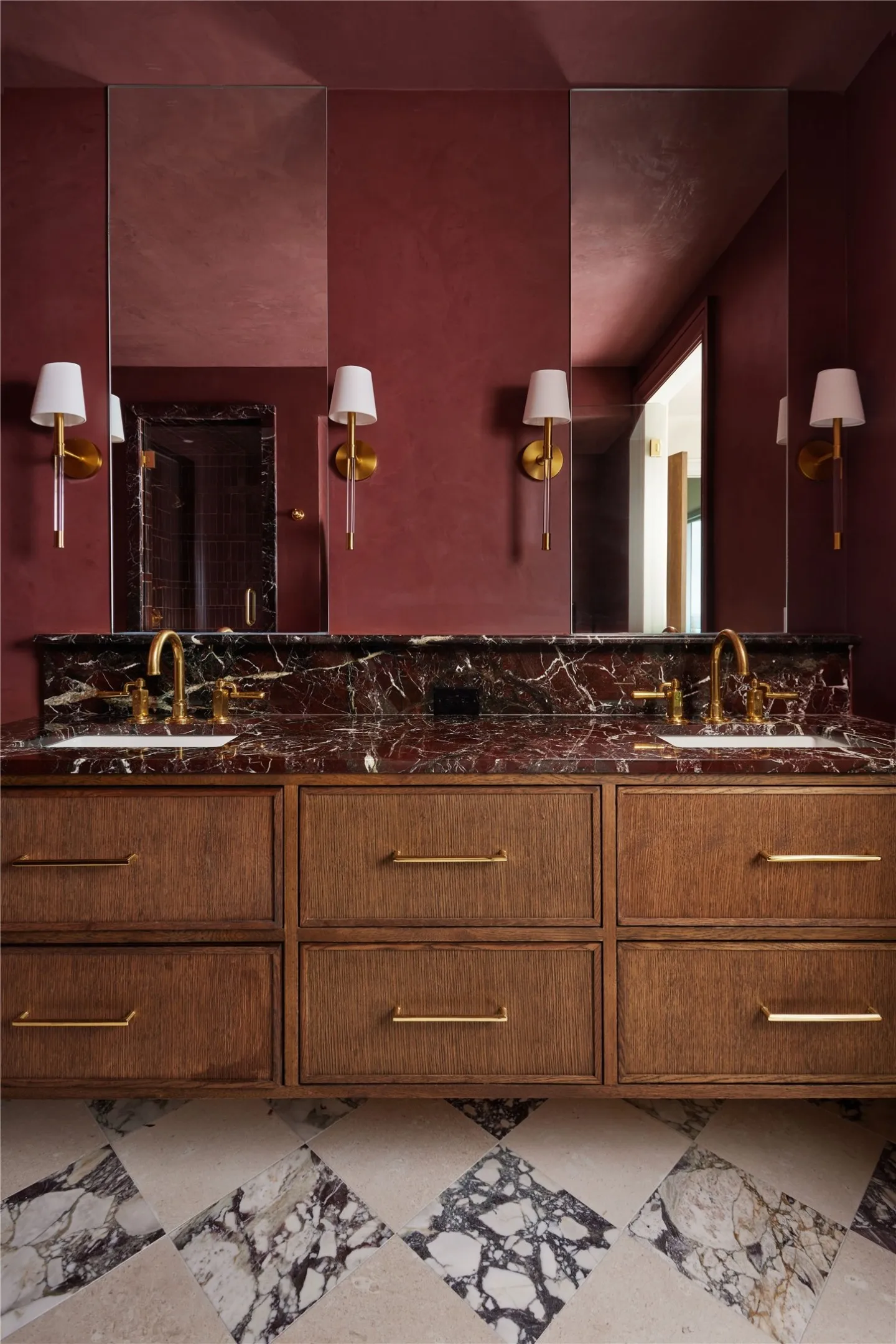 Double vanity with rich wood-finish cabinetry, a red-veined stone countertop, and dual brass faucets