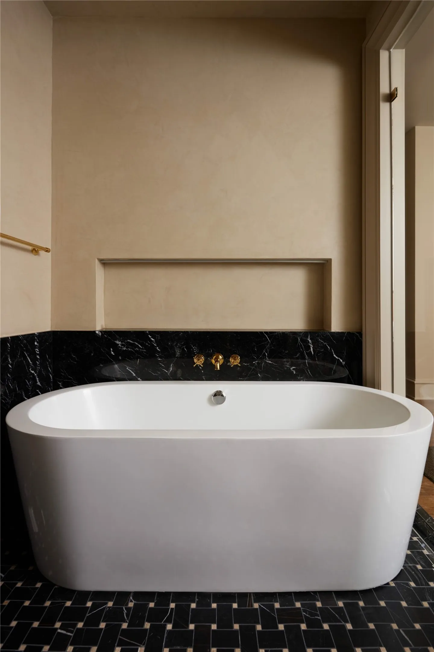 Freestanding soaking tub set against a black marble wainscoting