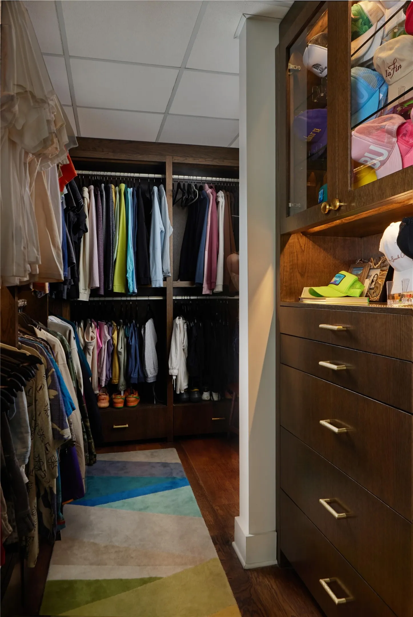 Custom-built closet system featuring extensive hanging storage, integrated drawers with gold-tone hardware, and glass-front display cabinetry