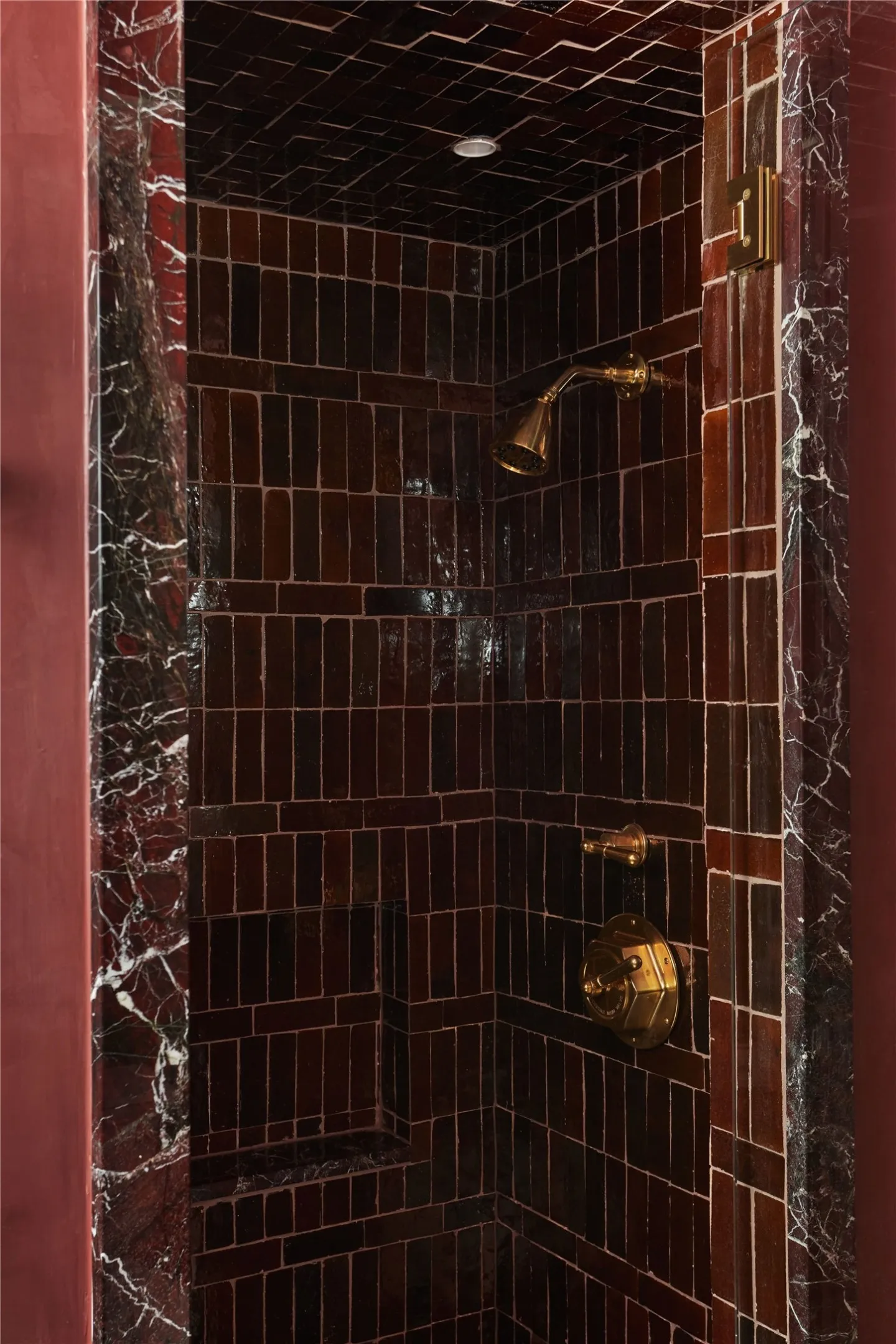Shower enclosure featuring dark brick-patterned tile, a built-in shower niche, and a gold-toned showerhead and controls