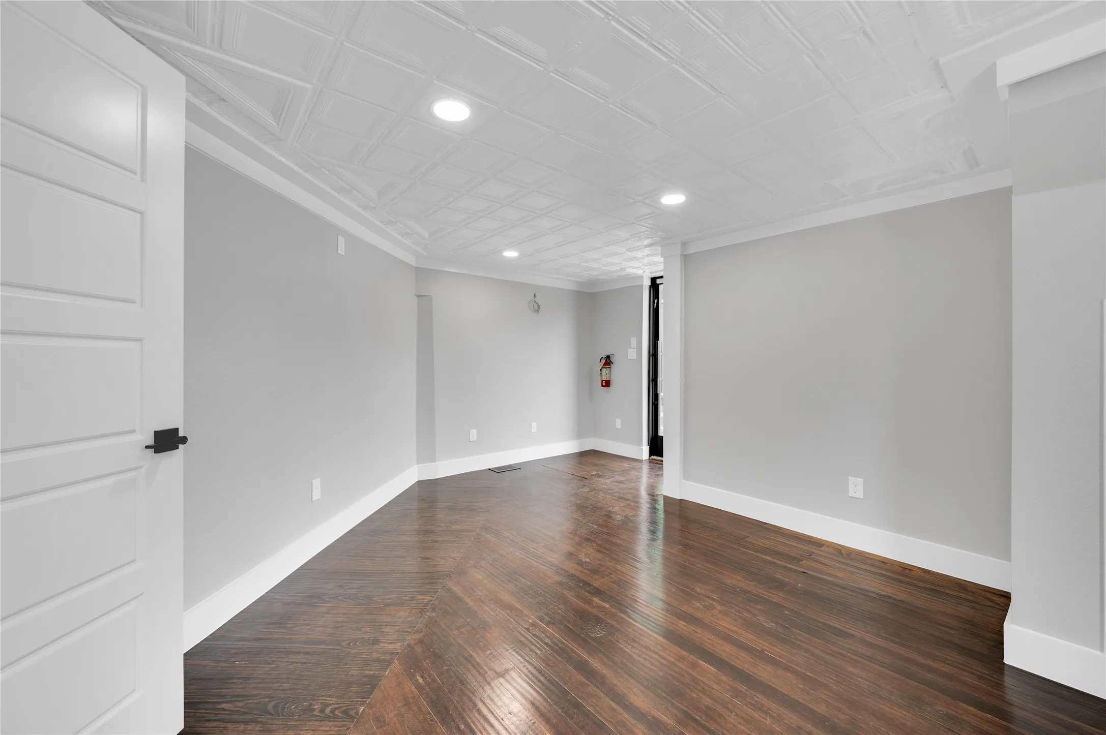Spacious room featuring wood-finish flooring, light grey walls, white baseboards, and crown molding